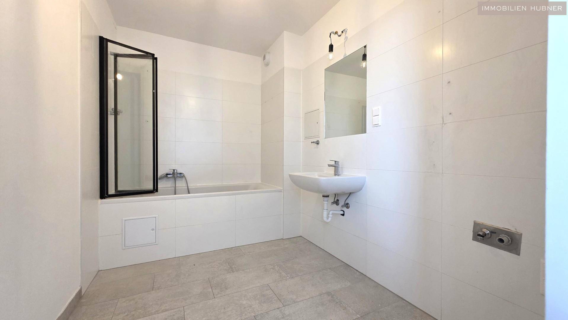 Modernes Badezimmer mit weißen Fliesen, Badewanne mit Duschwand und einem Waschbecken.