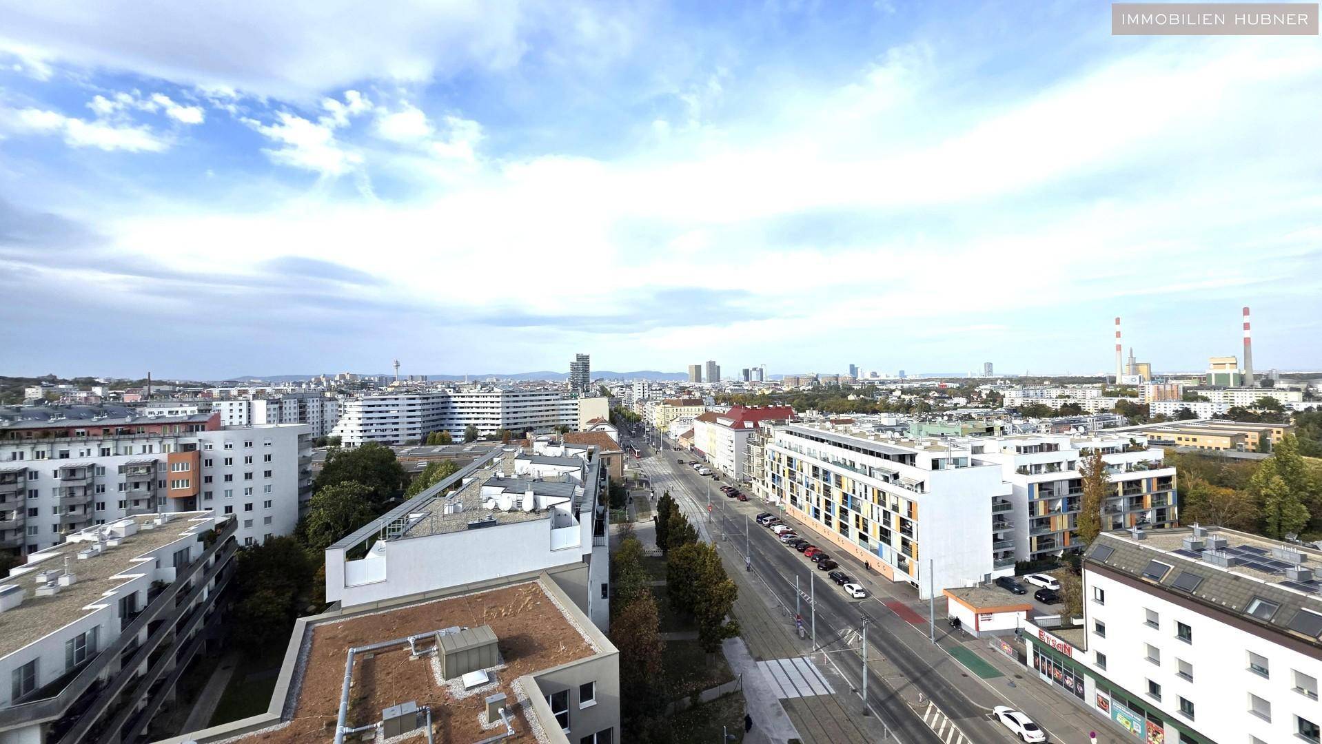 Weitläufiger Blick über die städtische Umgebung mit Wohngebäuden und Straßen unter blauem Himmel.