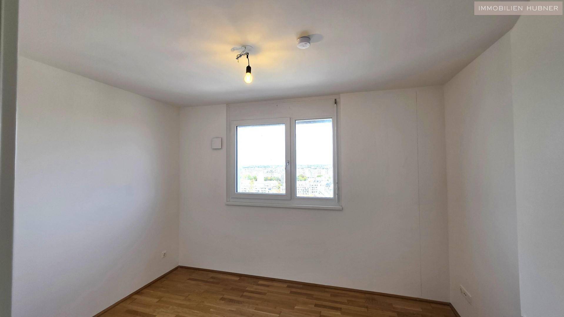 Helles Schlafzimmer mit Parkettboden und einem großen Fenster, das viel Tageslicht hereinlässt.