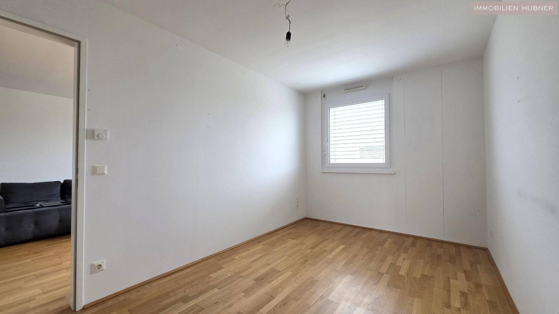 Helles Schlafzimmer mit Parkettboden und einem Fenster mit Jalousien, ideal für Ruhe.