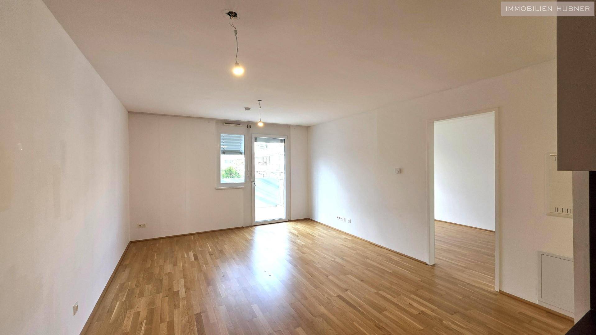 Geräumiges, helles Wohnzimmer mit Parkettboden und Fensterfront, bereit zur individuellen Gestaltung.