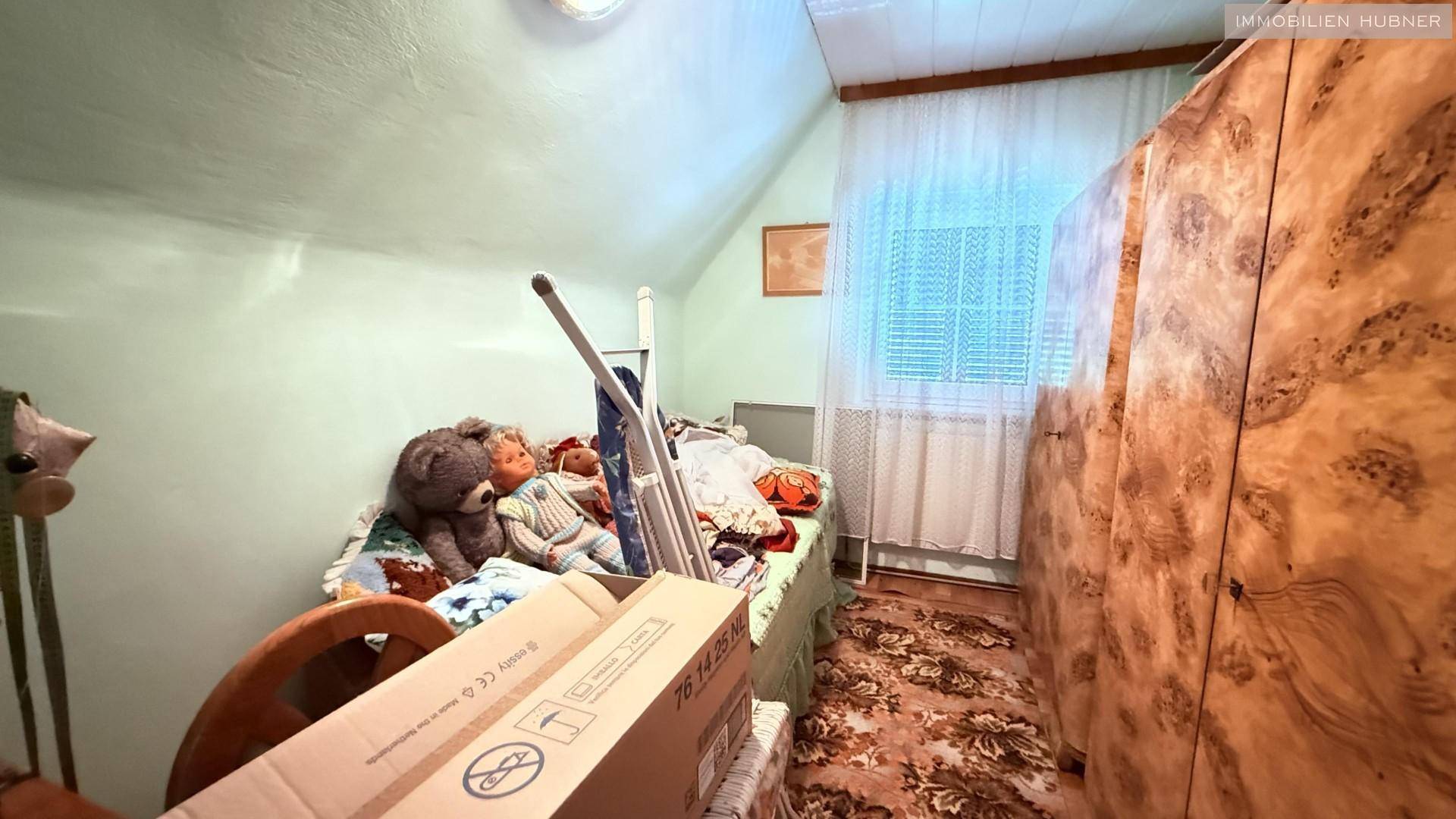 Kinderzimmer mit Bett, Spielzeug und einem großen Holzschrank.