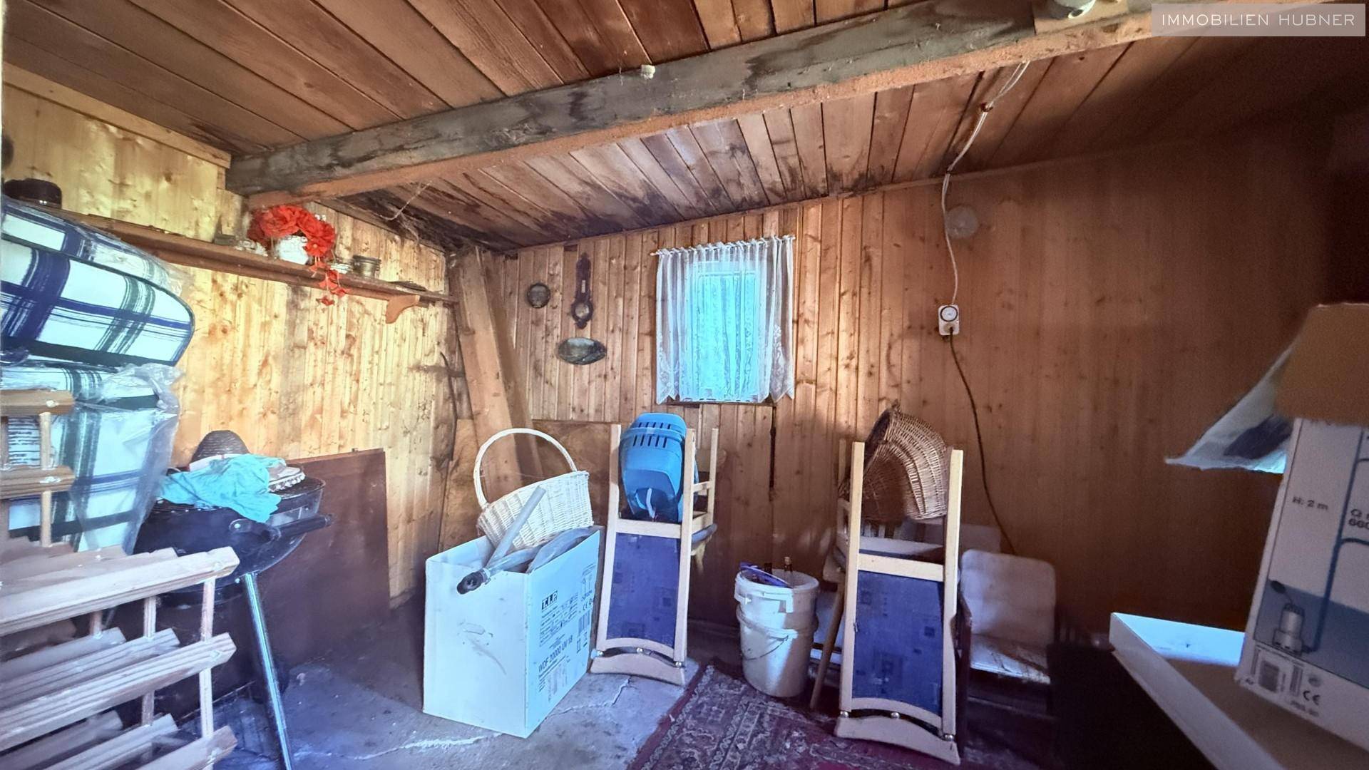 Rustikaler Abstellraum mit Holzverkleidung, Lagergegenständen und kleinem Fenster.
