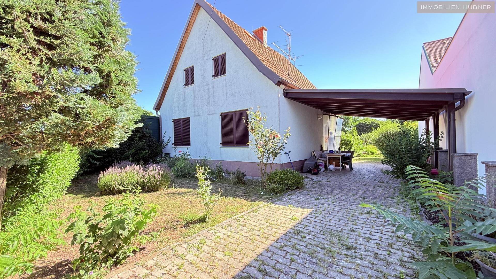 Hausfassade mit Garten, gepflasterter Auffahrt und einem überdachten Carport.