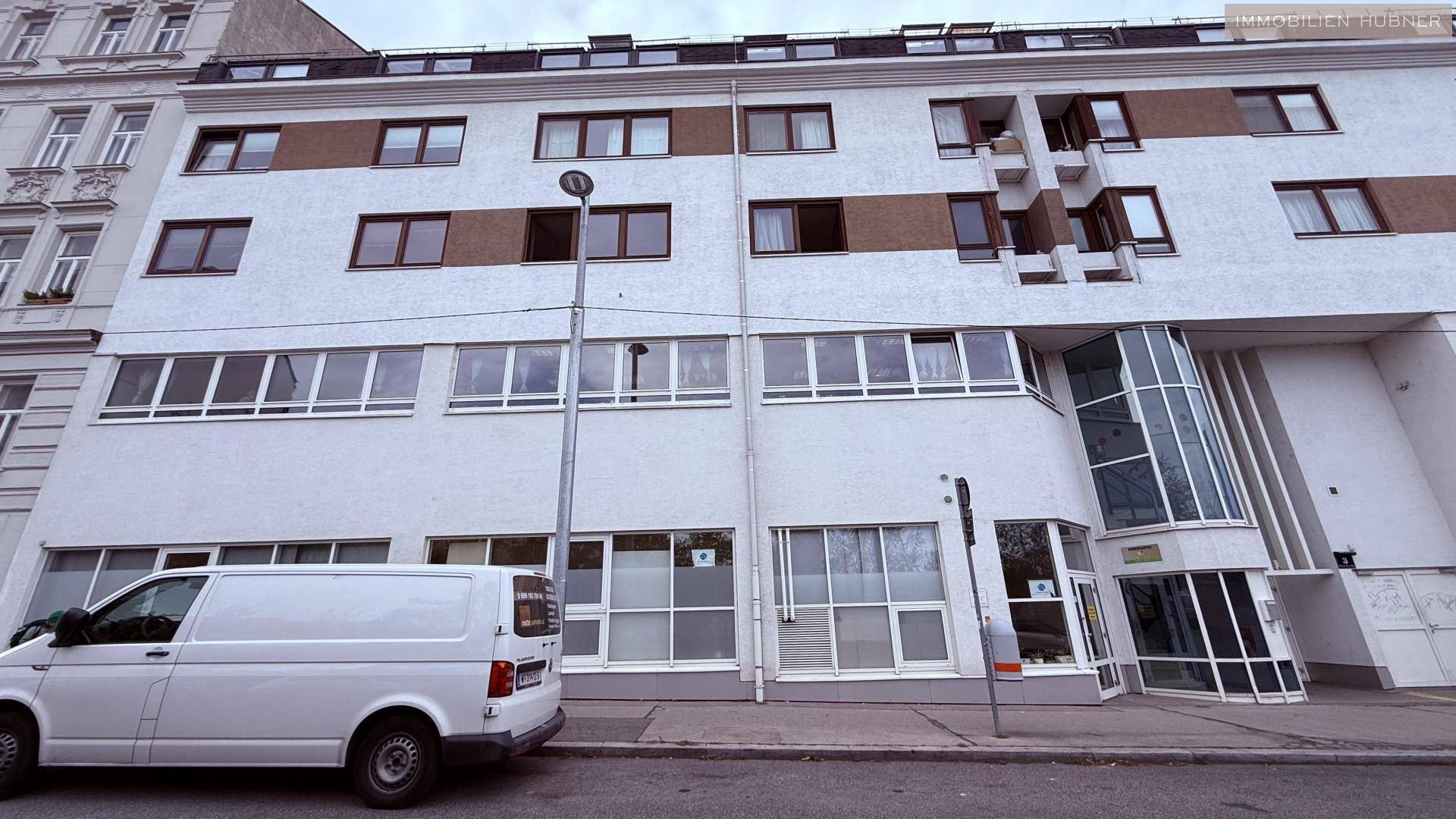 Mehrstöckiges Gebäude mit weißer Fassade, vielen Fenstern und einem modernen Eingangsbereich.