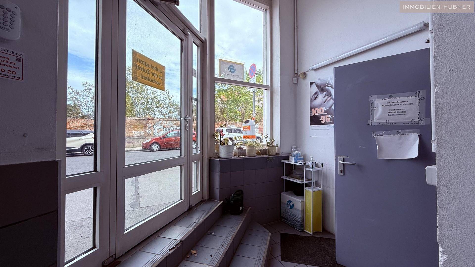 Eingangsbereich mit großen Glastüren und Fenstern, die zur Straße führen.