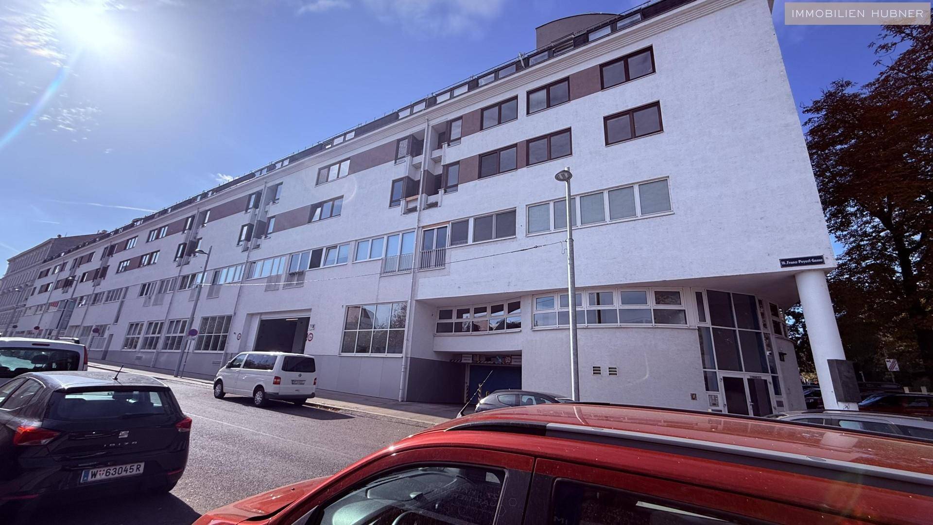 Weitläufiges Gebäude mit moderner Architektur, vielen Fenstern und parkenden Autos auf der Straße.