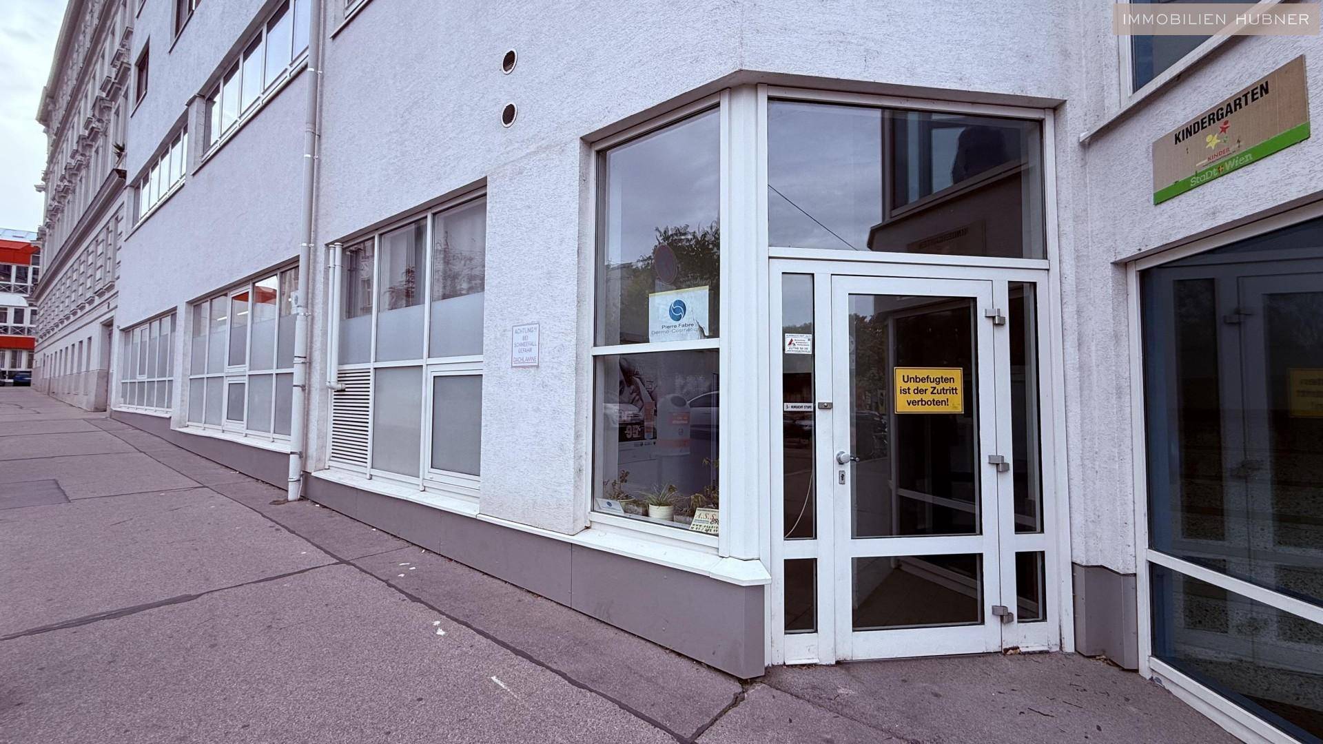 Eingangsbereich eines Gebäudes mit großen Glasfenstern und einer Tür, die zu einem Kindergarten führt.
