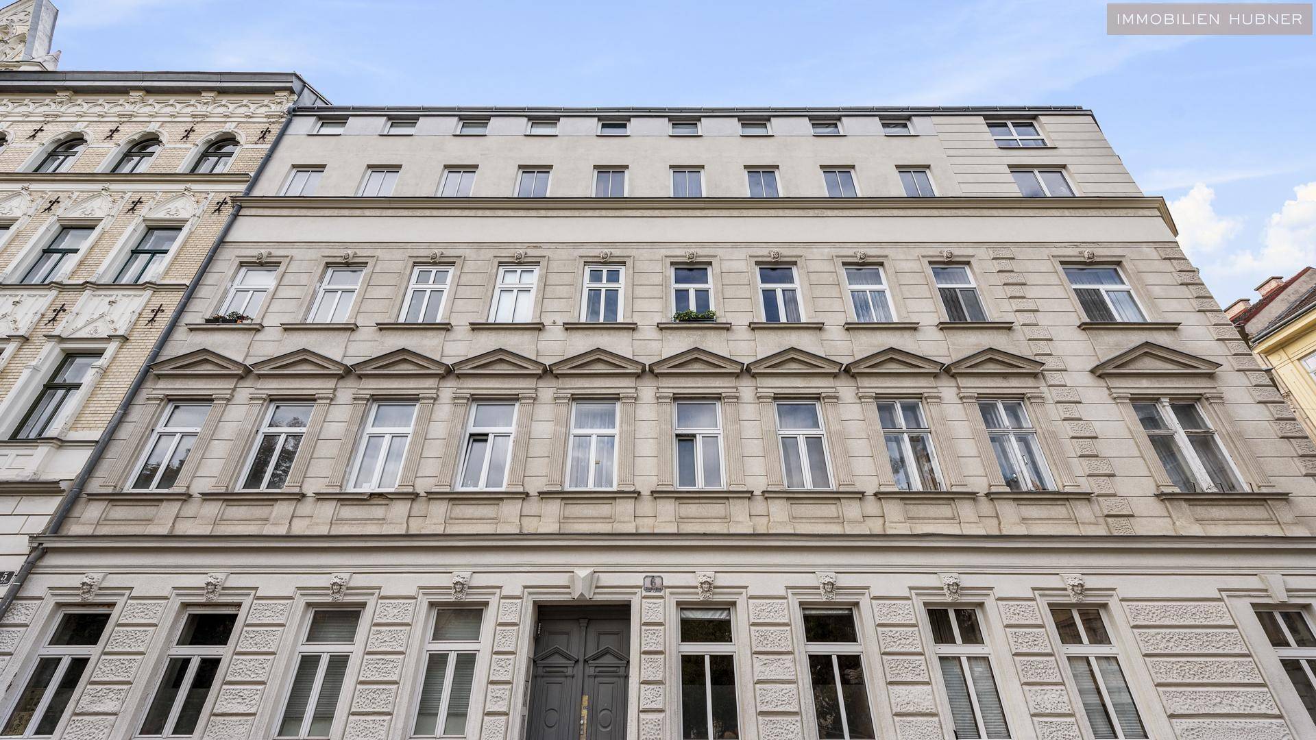 Historische Fassade eines Mehrfamilienhauses mit vielen Fenstern und dekorativen Elementen.