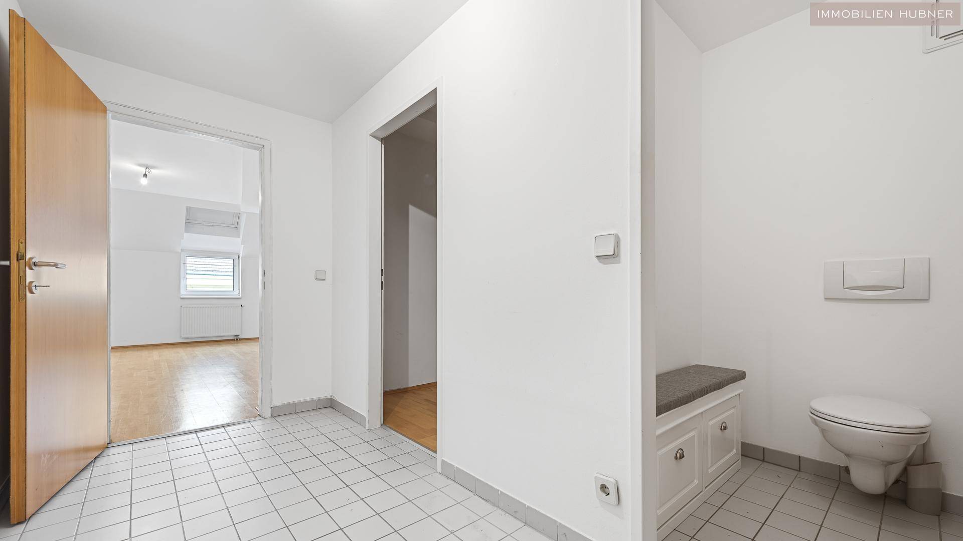 Eingangsbereich mit Fliesenboden, Sitzbank und Zugang zu einem separaten WC.