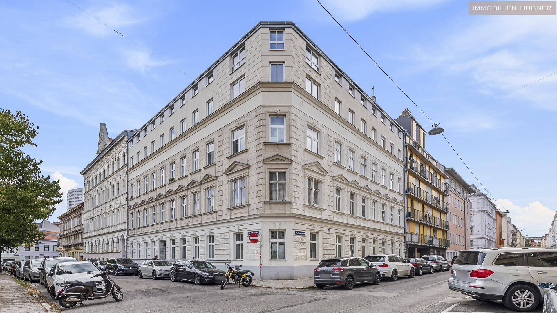 Eckgebäude in der Stadt mit klassischer Architektur und parkenden Autos auf der Straße.