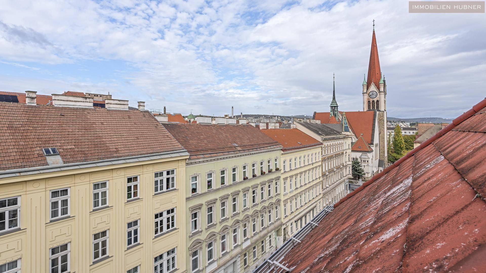 Panoramablick über die Dächer der Stadt mit historischer Kirche und Wohngebäuden unter bewölktem Himmel.