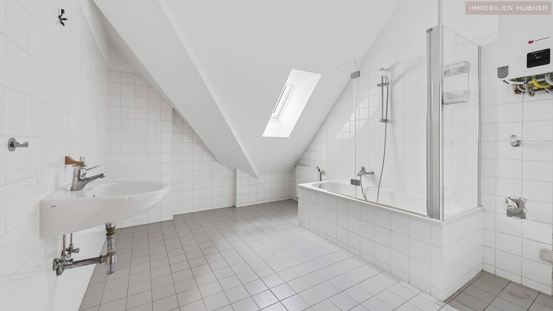 Gefliestes Badezimmer im Dachgeschoss mit Badewanne, Dusche und Dachfenster für natürliches Licht.