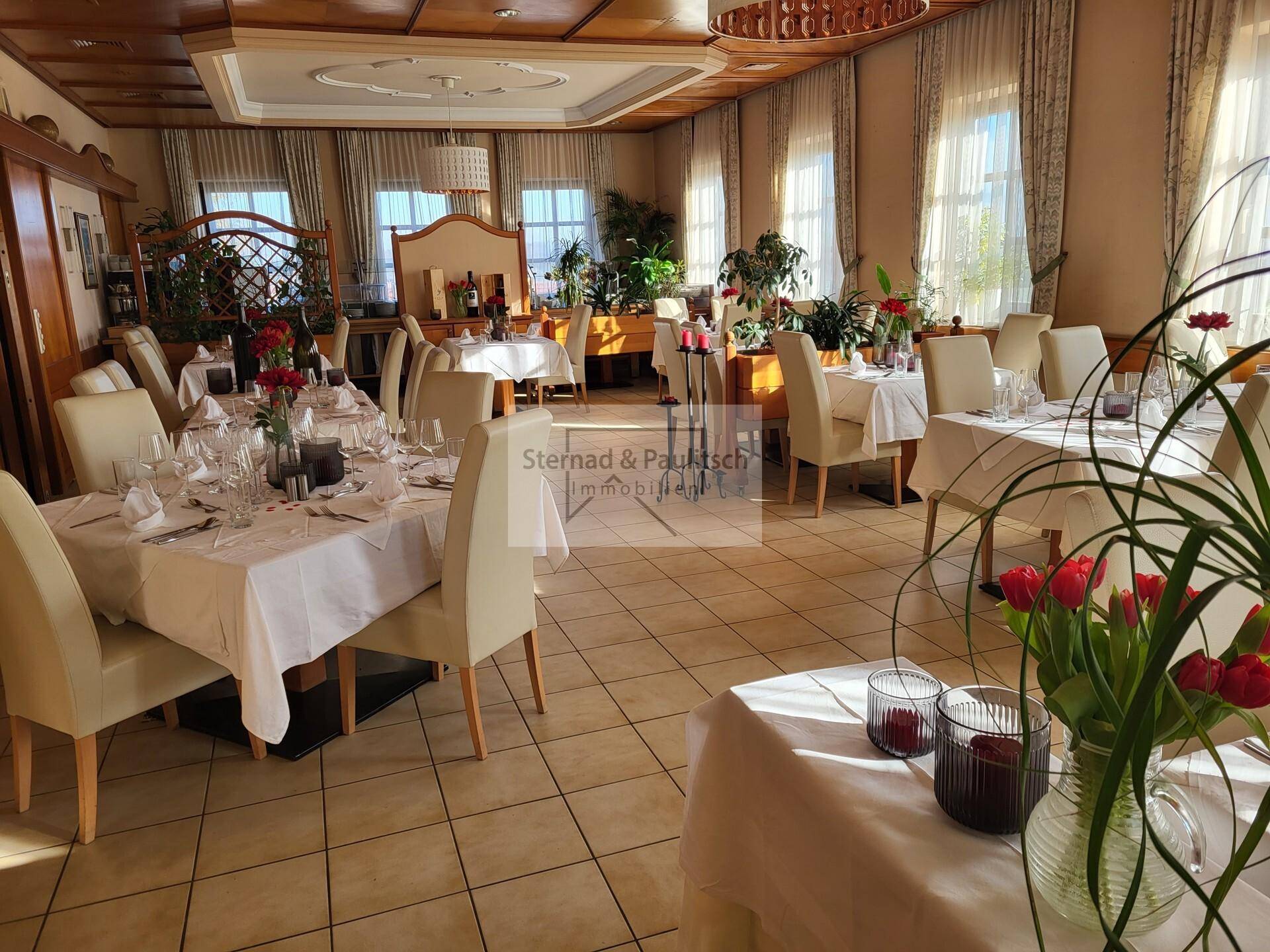 Heller Speisesaal mit mehreren Tischen, elegant gedeckt und mit Pflanzen dekoriert.