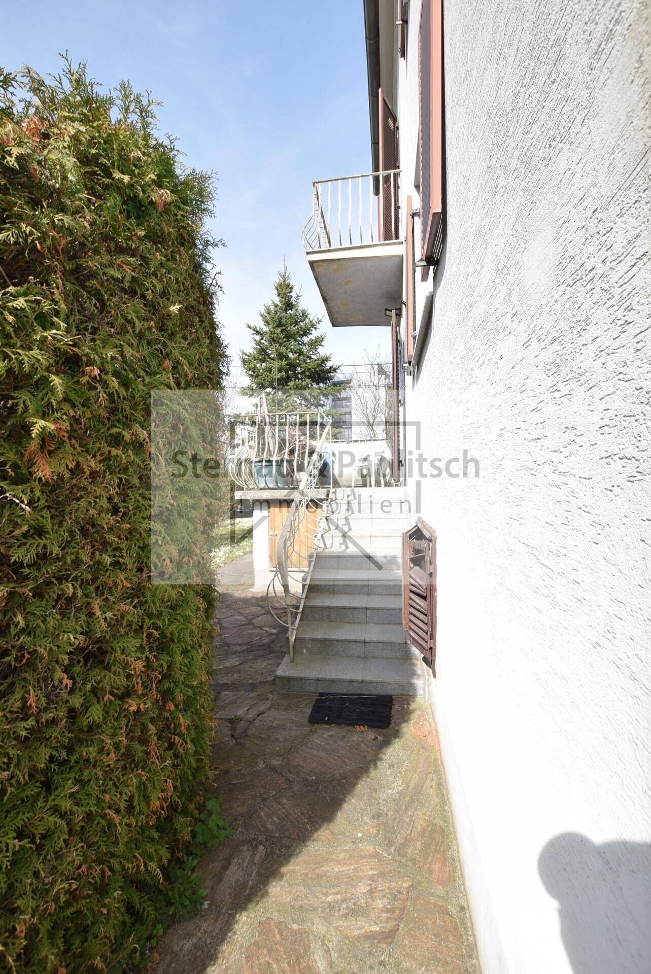 Seitlicher Zugang zum Haus mit Treppe und Blick auf den Balkon.