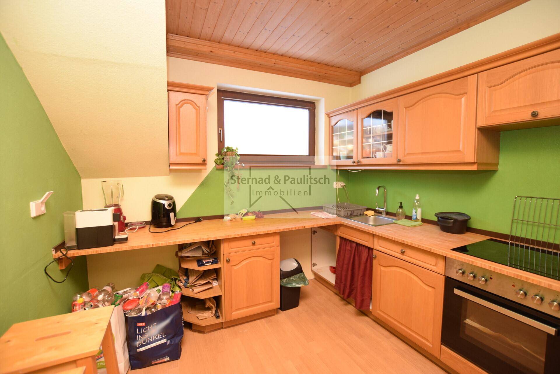 Dachgeschossküche mit Holzschränken, grünen Wänden und Fenster, funktional eingerichtet.