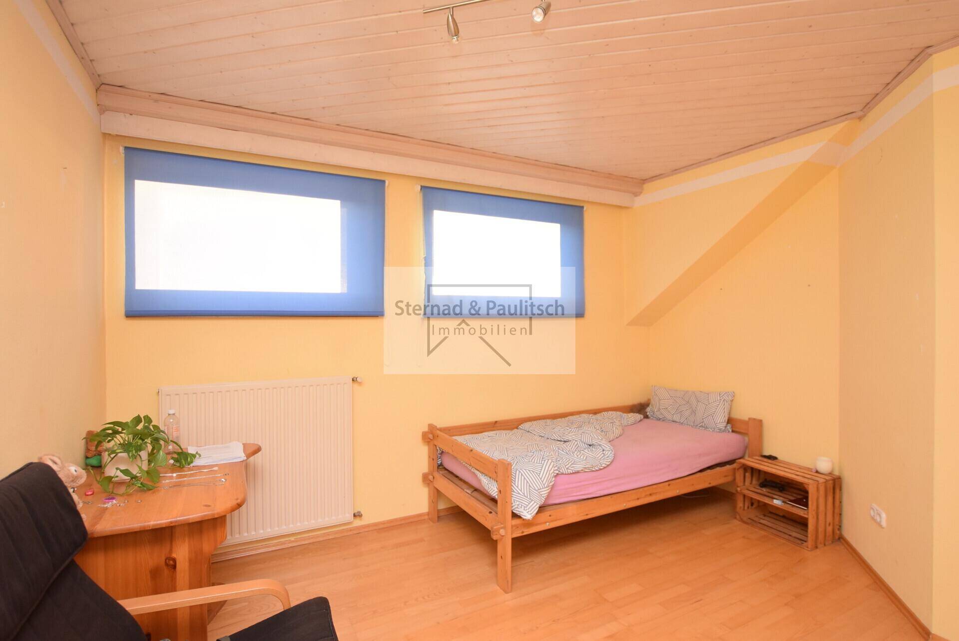 Dachgeschosszimmer mit Einzelbett, Schreibtisch und gelben Wänden, bietet vielseitige Nutzung.