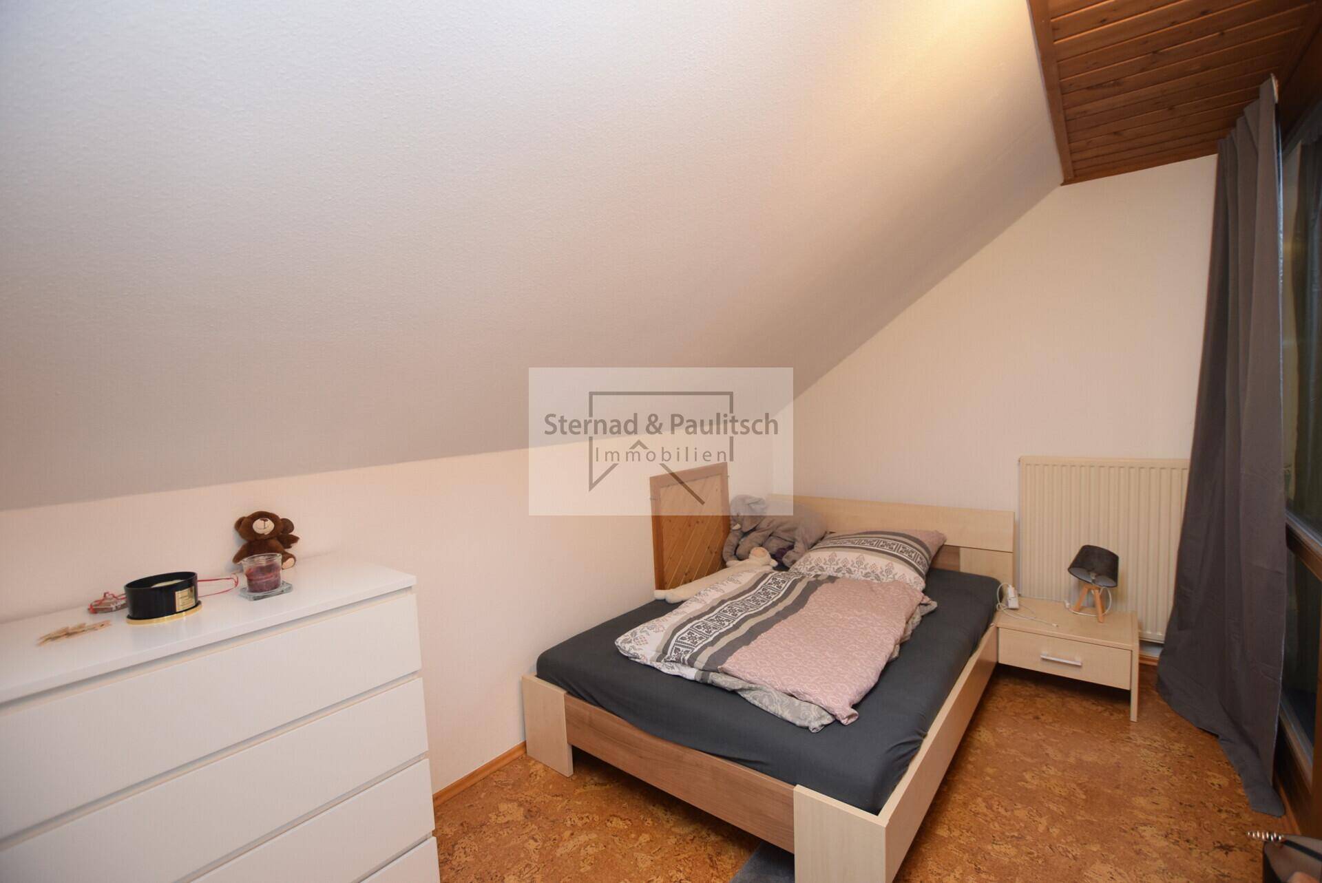 Schlafzimmer im Dachgeschoss mit schräger Decke und Korkboden, einfach und funktional eingerichtet.