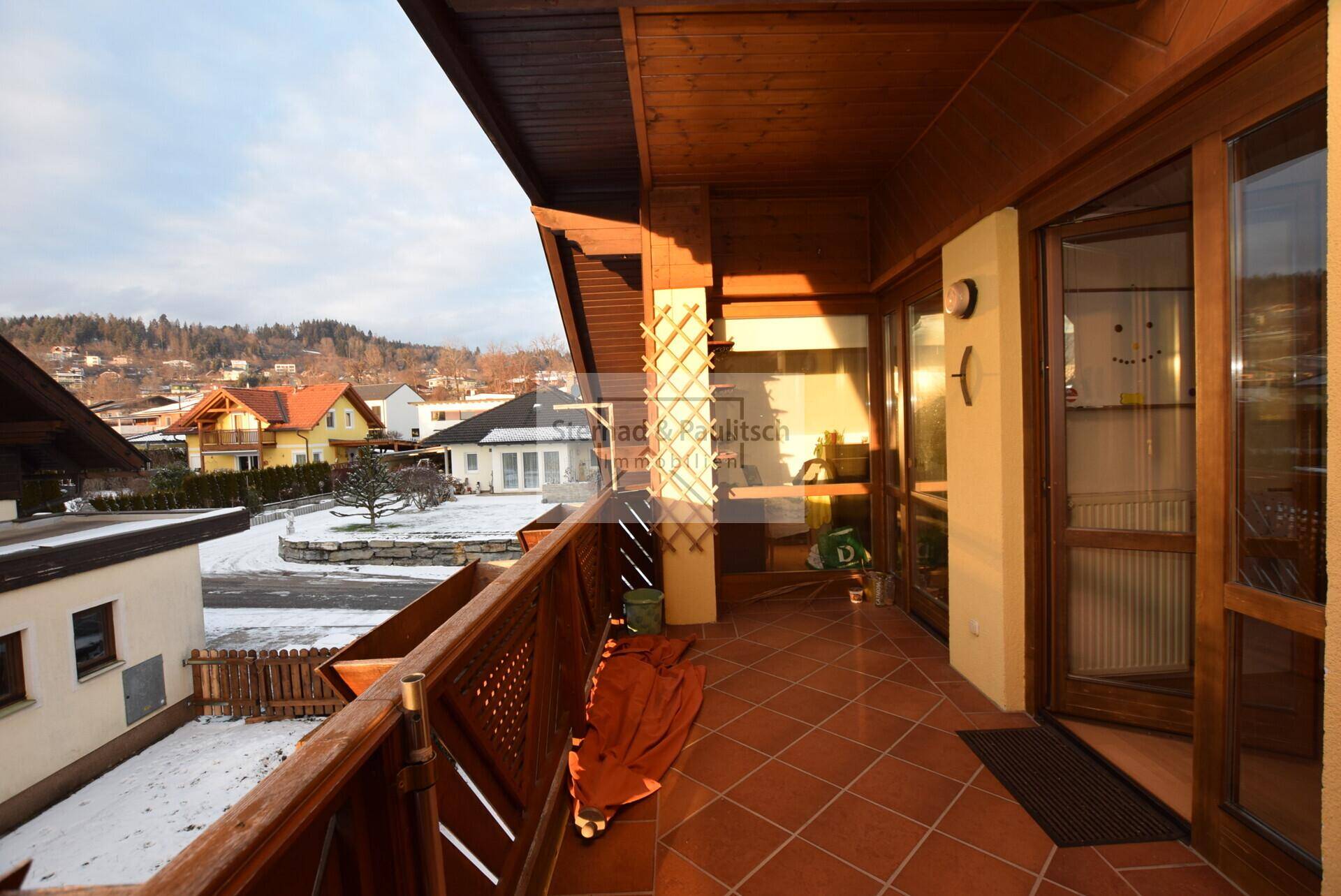 Überdachter Balkon mit Fliesenboden und Holzgeländer, bietet einen Blick auf die verschneite Umgebung.