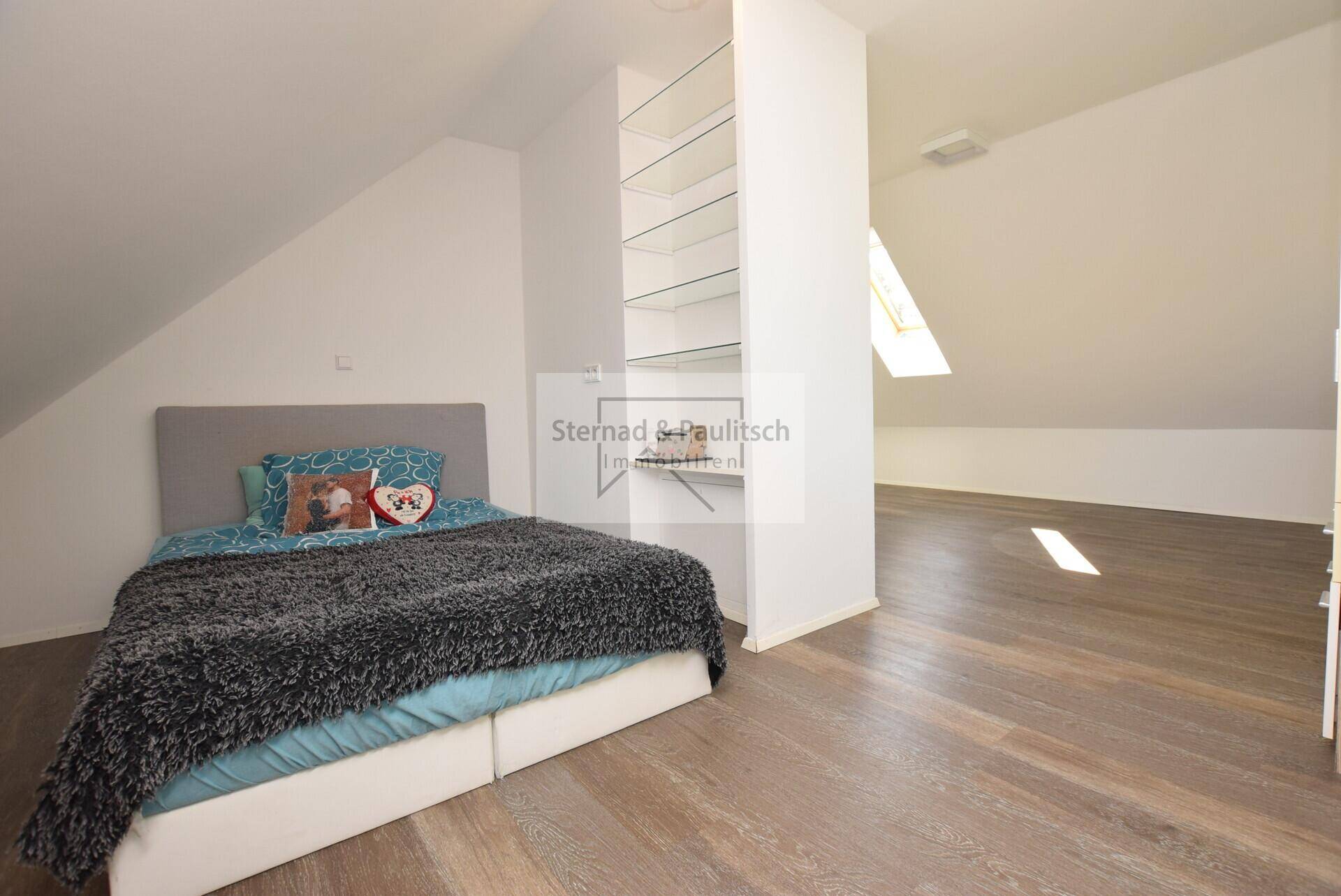 Gemütliches Schlafzimmer im Dachgeschoss mit Bett, Regal und Laminatboden.
