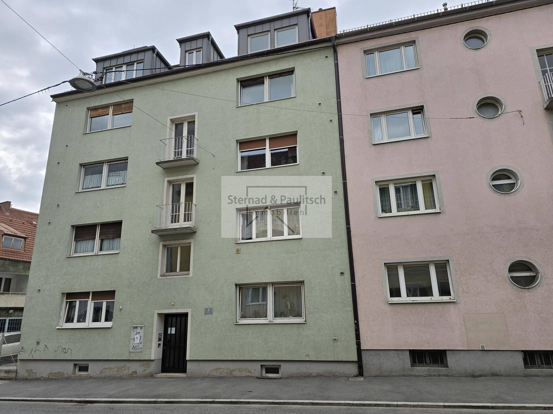 Mehrfamilienhaus mit grüner und rosa Fassade, ausgestattet mit Fenstern und kleinen Balkonen.