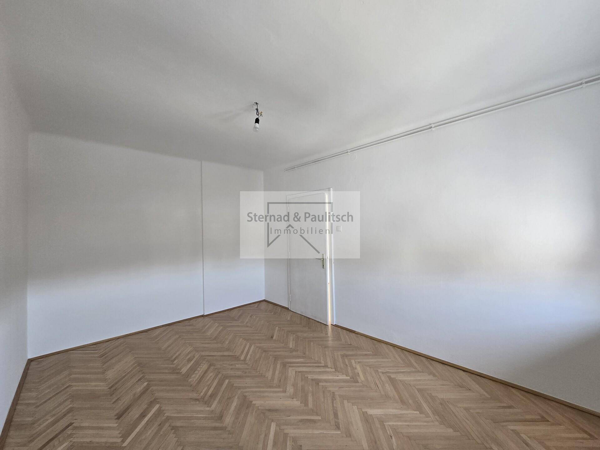 Geräumiges Zimmer mit Fischgrätparkett und integrierten Wandschränken, ideal für Stauraum.