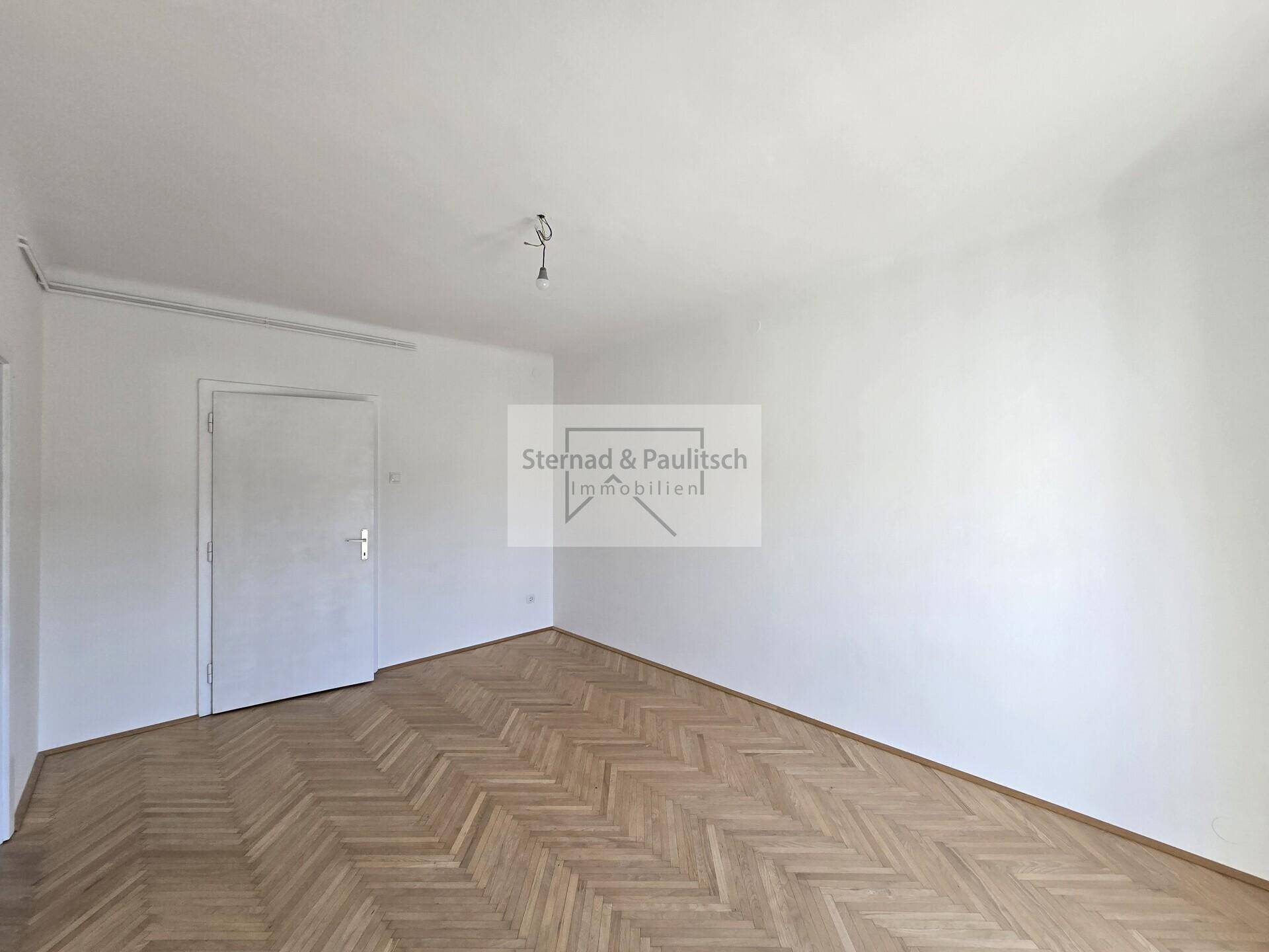 Einfaches Zimmer mit Fischgrätparkettboden und einer weißen Tür, bereit zur individuellen Gestaltung.