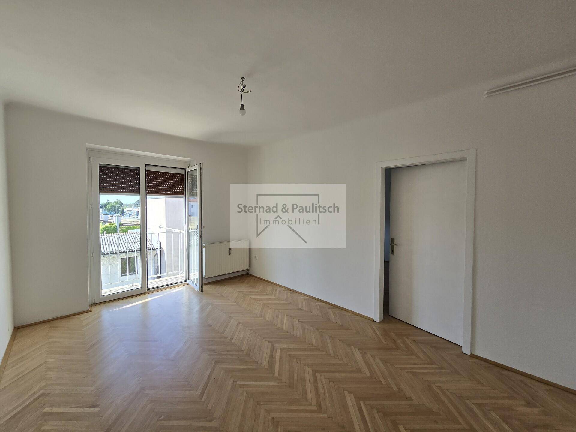 Geräumiges Zimmer mit Fischgrätparkett und Zugang zu einem französischen Balkon, der viel Licht hereinlässt.