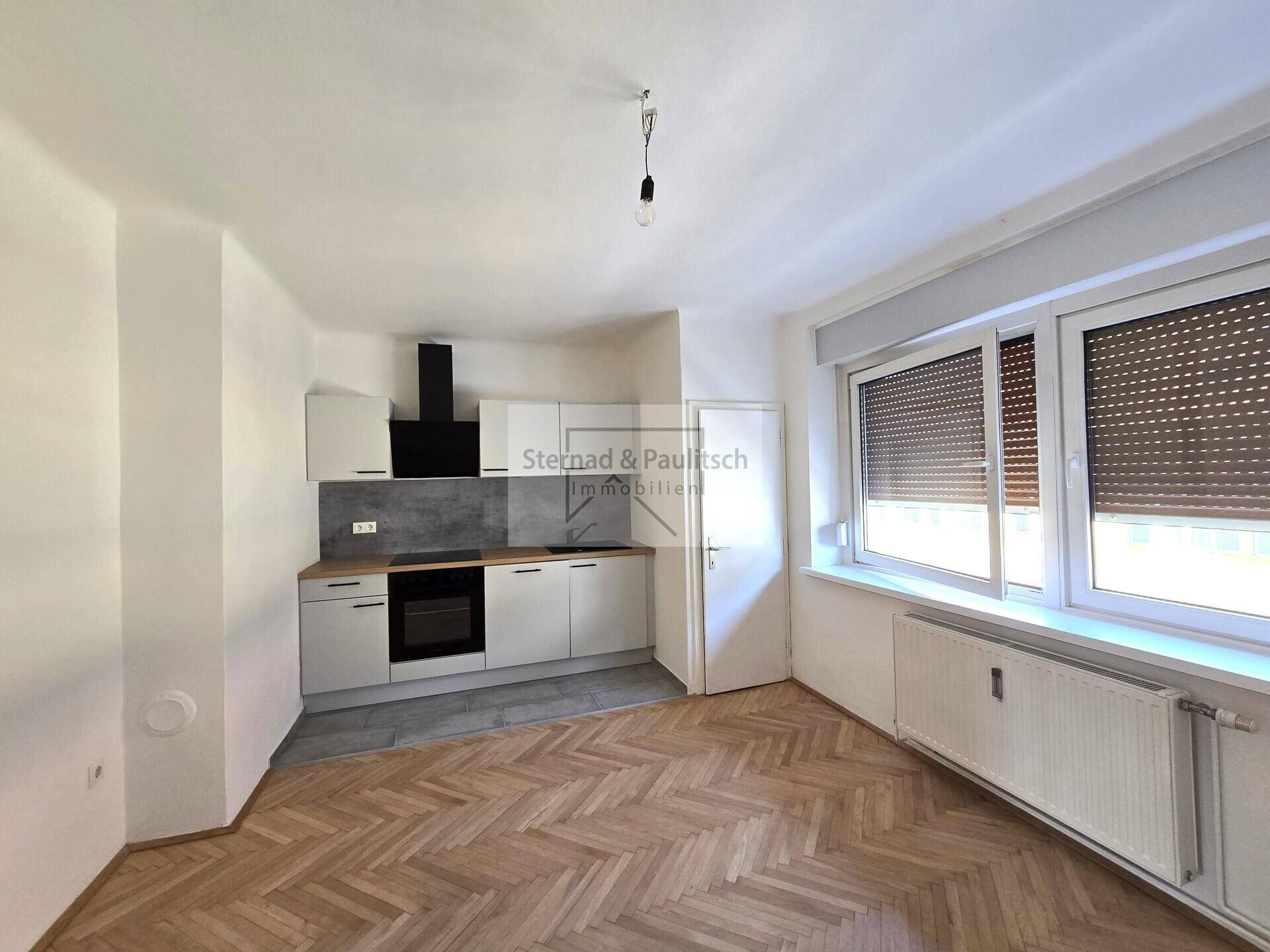 Moderne Küchenzeile mit grauen Fronten und Holz-Arbeitsplatte in einem hellen Raum mit Parkettboden.