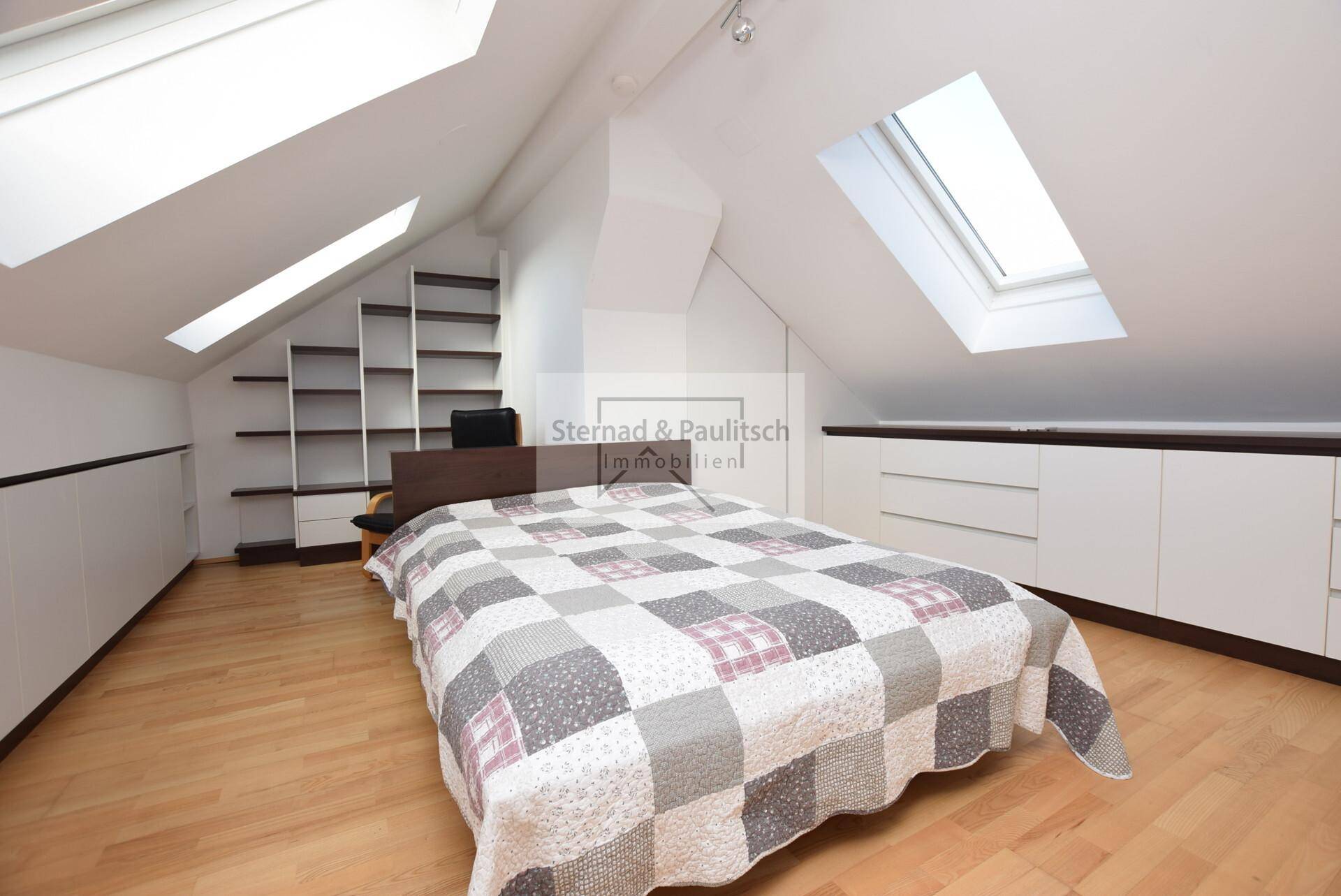 Dachgeschoss-Schlafzimmer mit Holzboden, Einbauschränken und Dachfenstern für viel Licht.