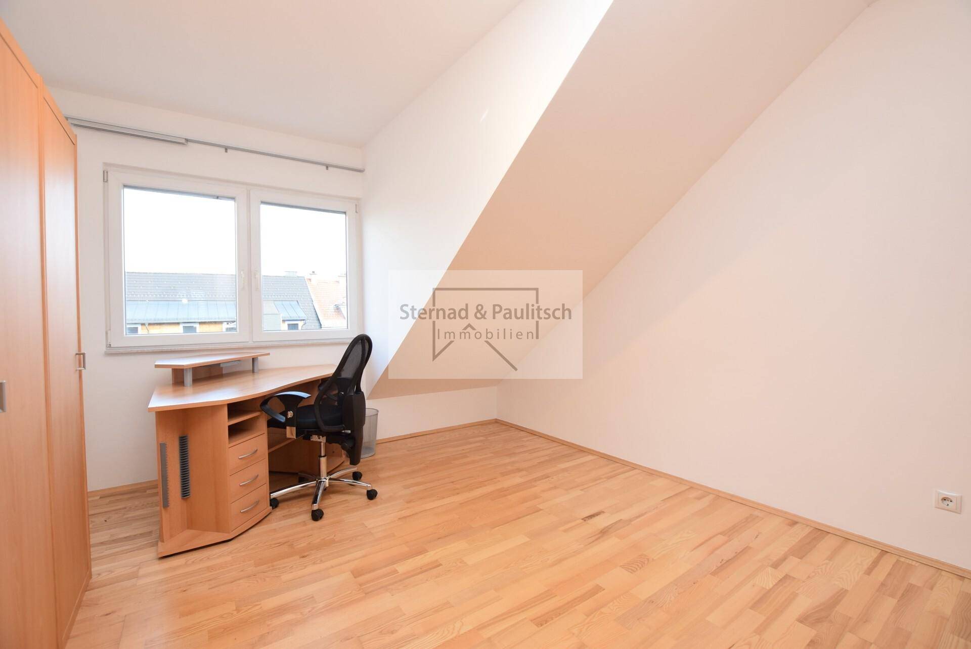 Helles Arbeitszimmer mit Holzboden, Schreibtisch und Fenster unter schräger Dachfläche.