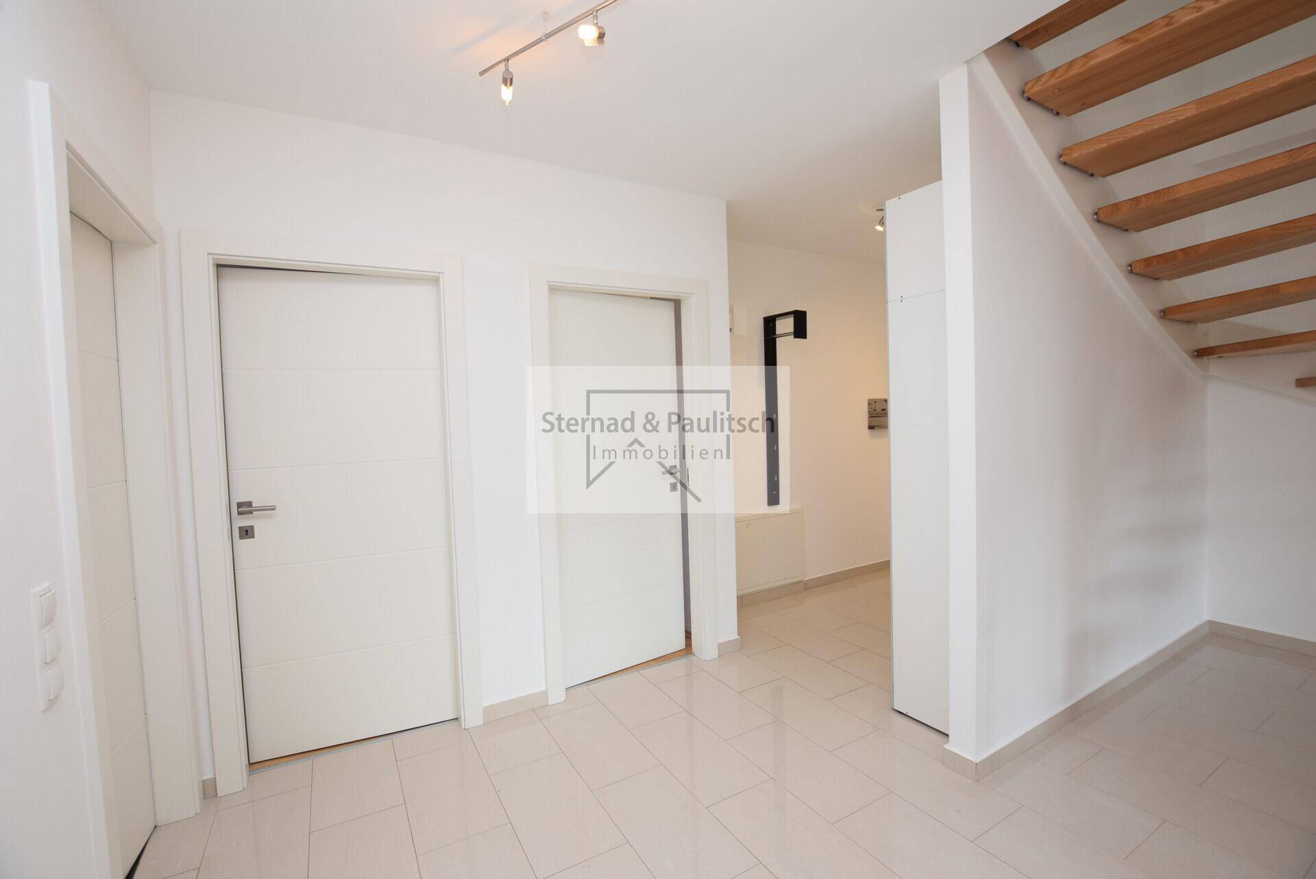 Heller Flur mit Fliesenboden und einer modernen Holztreppe, die in die obere Etage führt.
