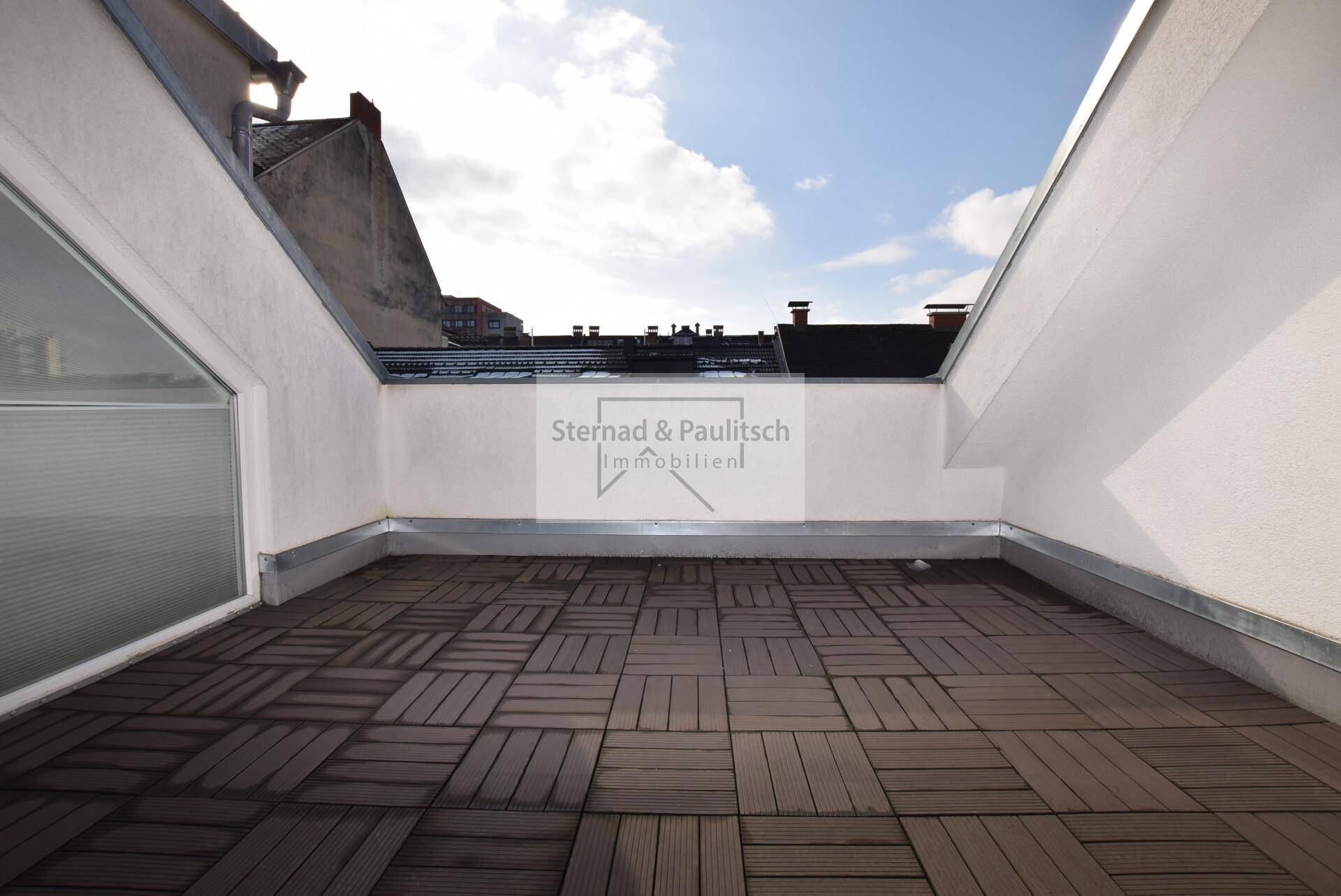 Geräumige Dachterrasse mit Holzdielen und Blick auf die umliegenden Dächer.