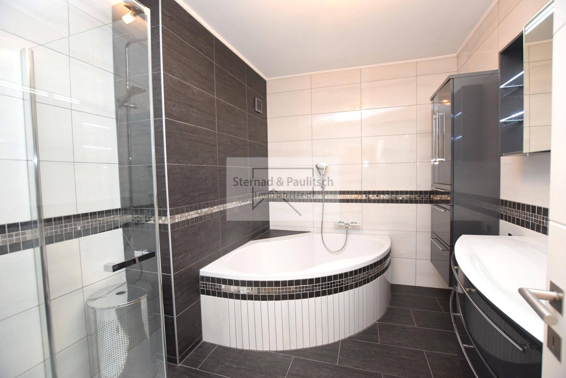 Modernes Badezimmer mit dunklen Fliesen, Eckbadewanne und separater Duschkabine.