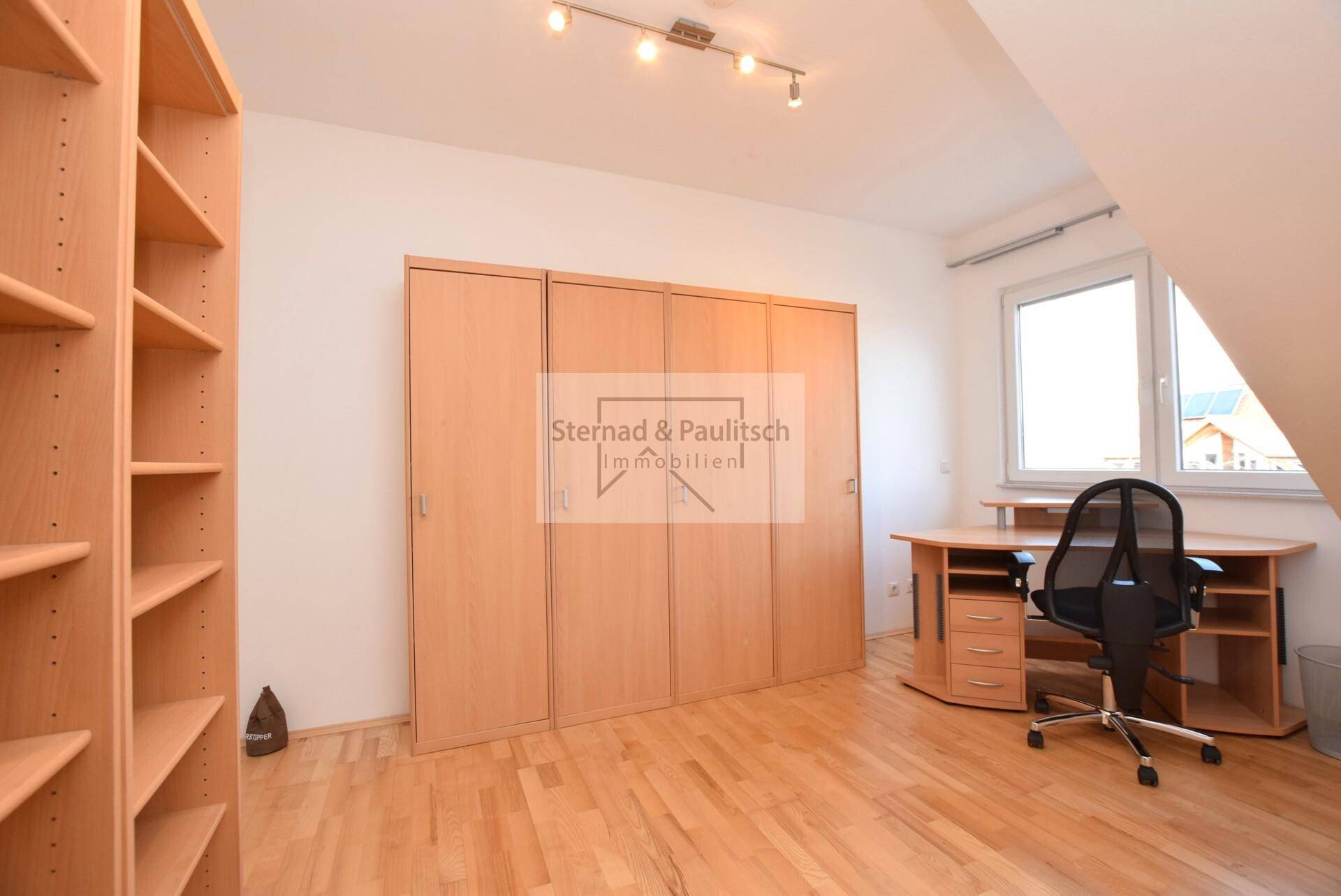 Arbeitszimmer mit Holzboden, großem Kleiderschrank und Schreibtisch am Fenster.