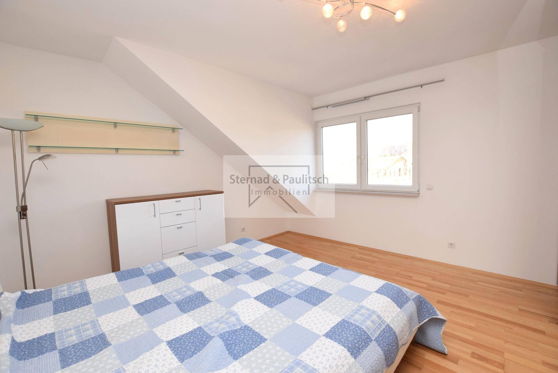 Helles Schlafzimmer mit Holzboden, Fenster und schrägen Wänden im Dachgeschoss.