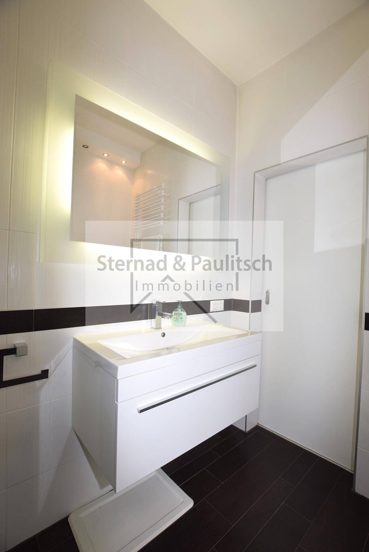 Modernes Badezimmer mit stilvollem Waschtisch, beleuchtetem Spiegel und Handtuchheizkörper.