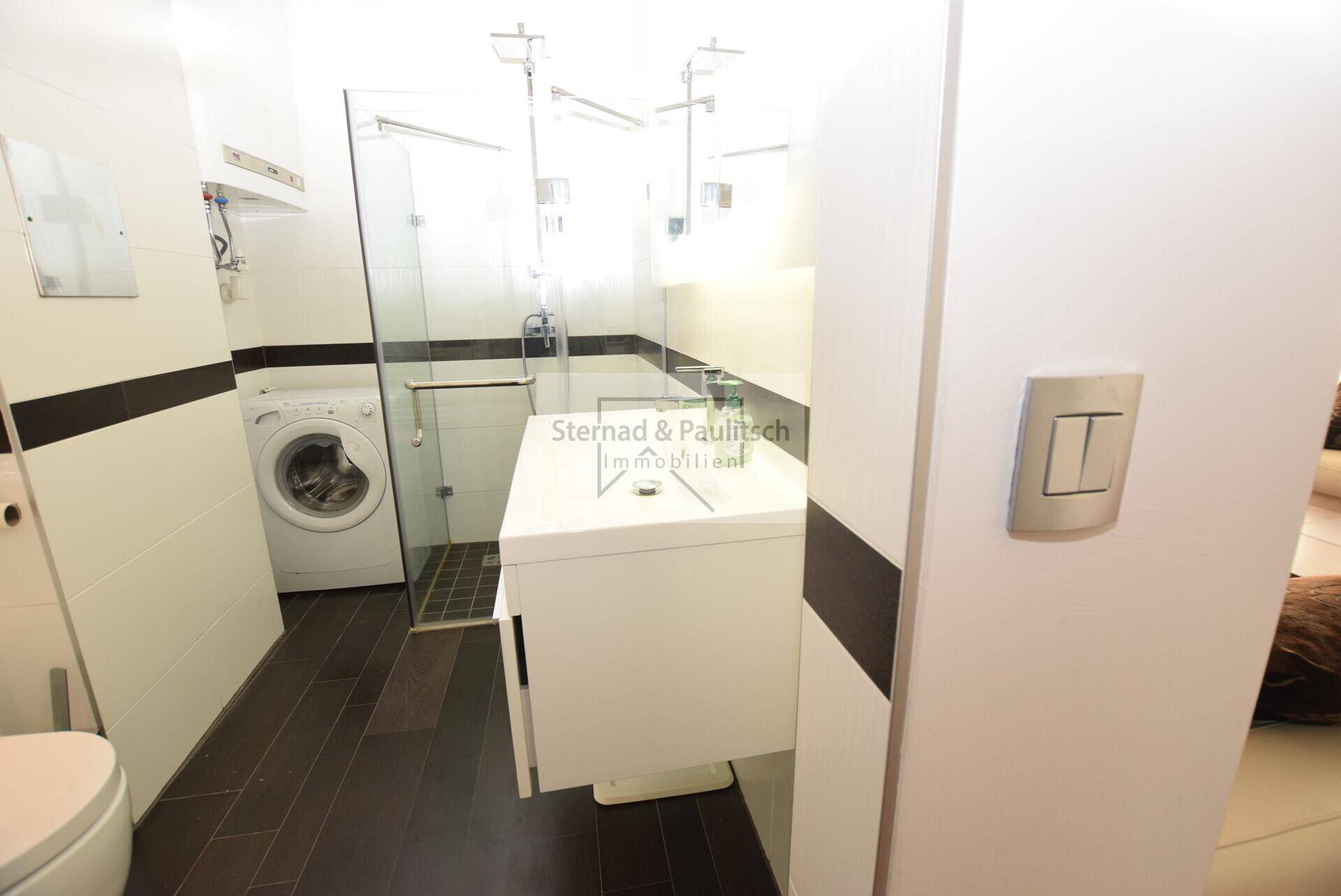 Modernes Badezimmer mit Dusche, Waschbecken, WC und integrierter Waschmaschine.