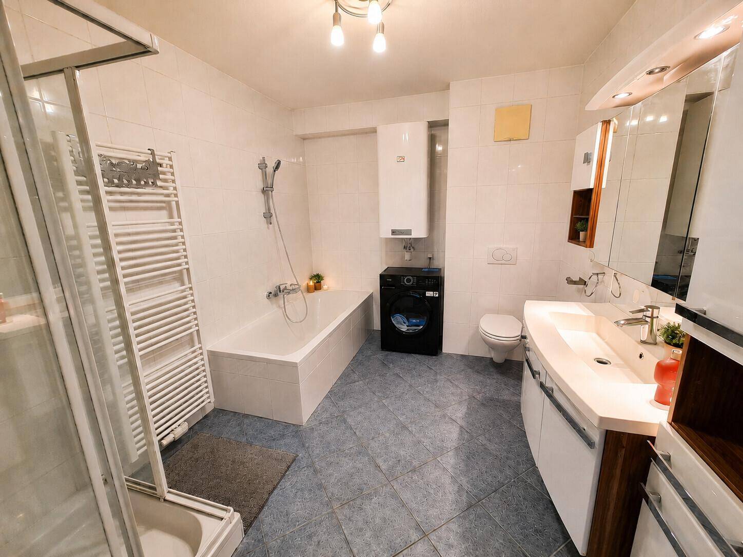 Gefliestes Badezimmer mit Badewanne, Dusche, Waschmaschine und einem Doppelwaschbecken.