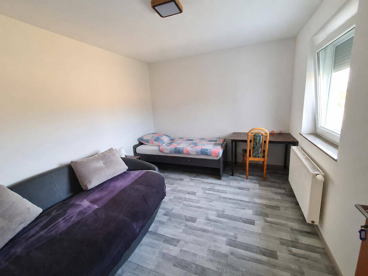 Gemütliches Schlafzimmer mit Einzelbett, Sofa und Schreibtisch, funktional und hell eingerichtet.