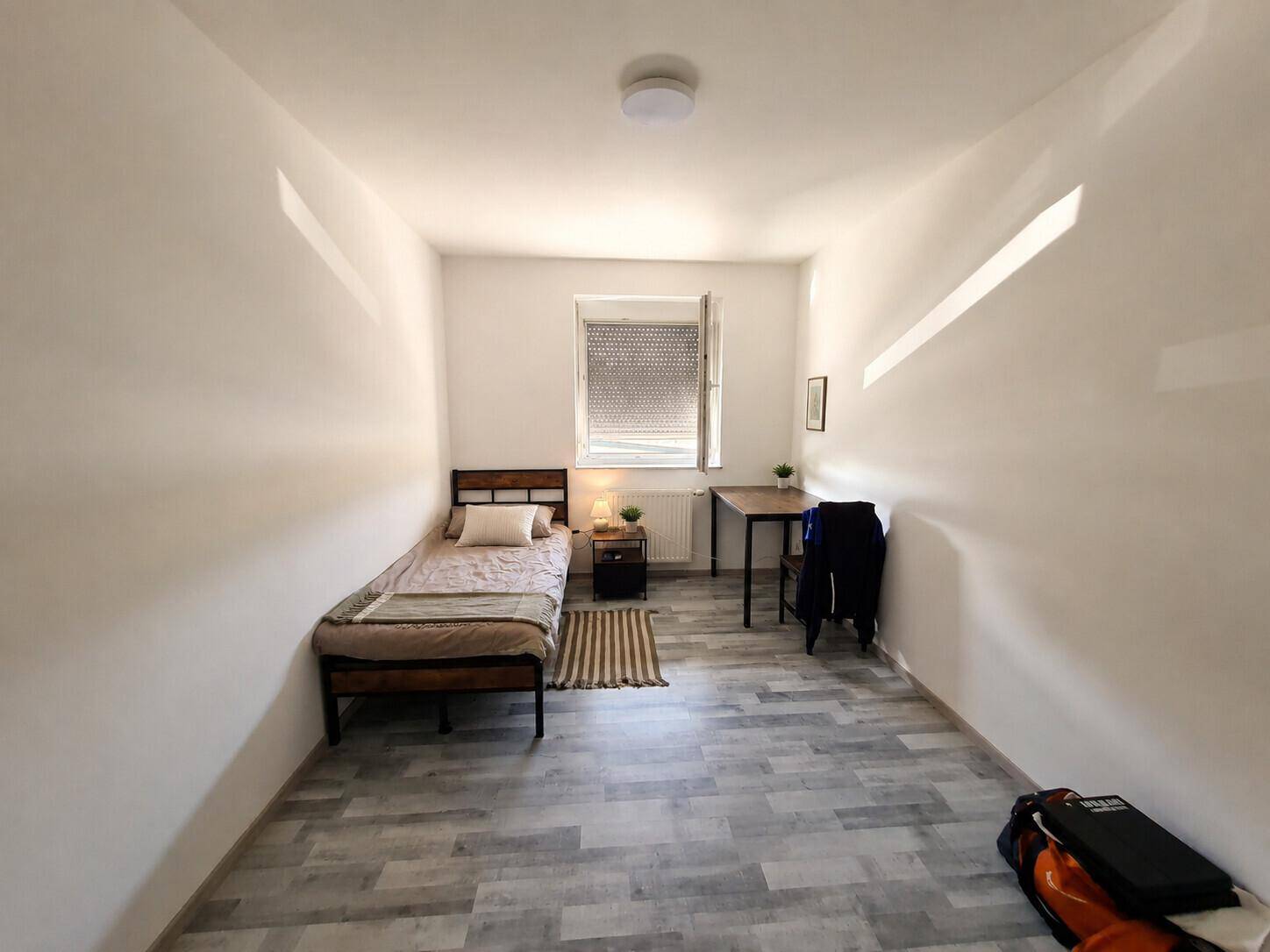 Schlichtes und helles Schlafzimmer mit Einzelbett, kleinem Schreibtisch und Laminatboden.