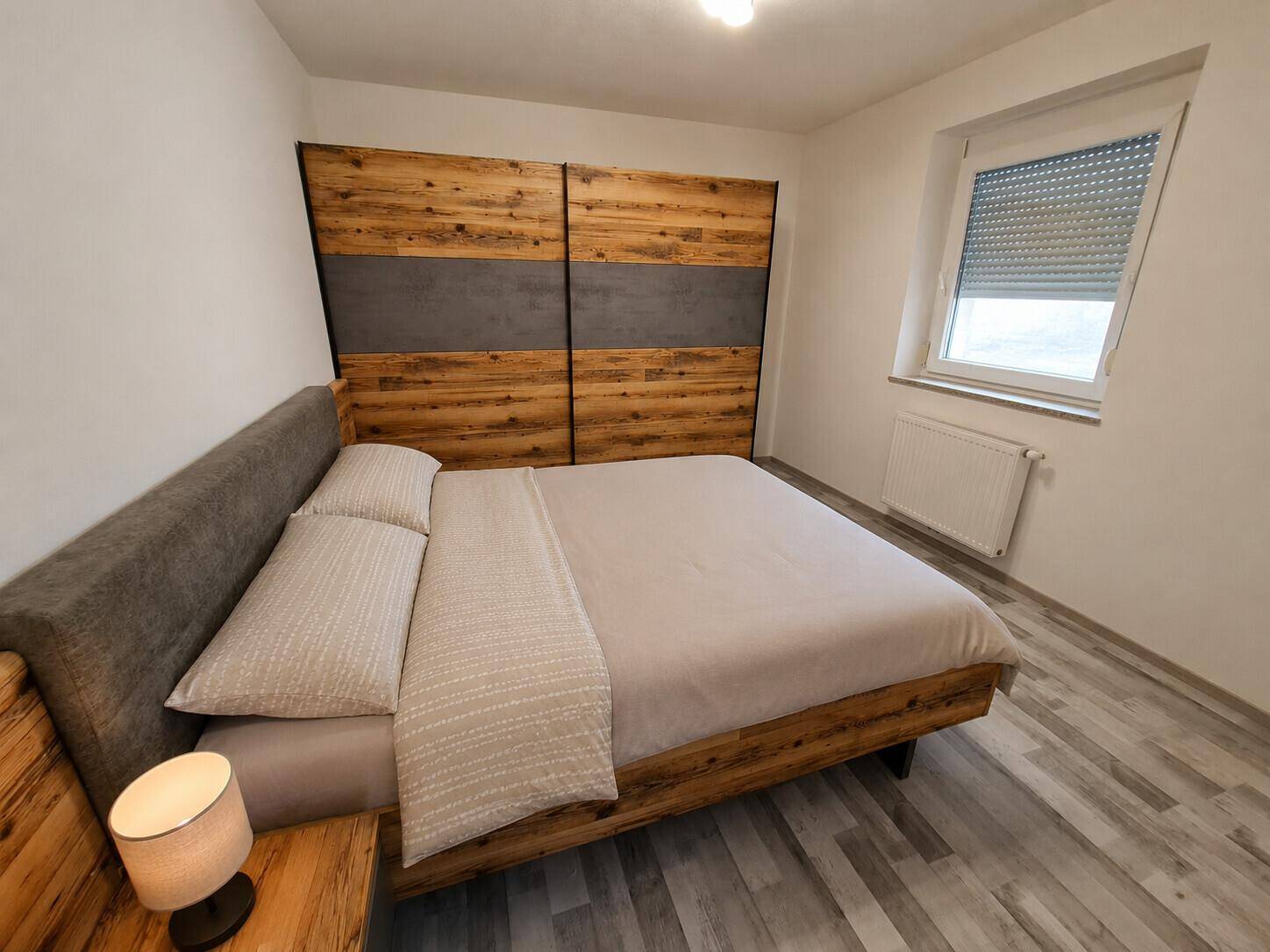 Schlafzimmer mit Doppelbett und einem großen Holzschrank, ergänzt durch hellen Laminatboden.