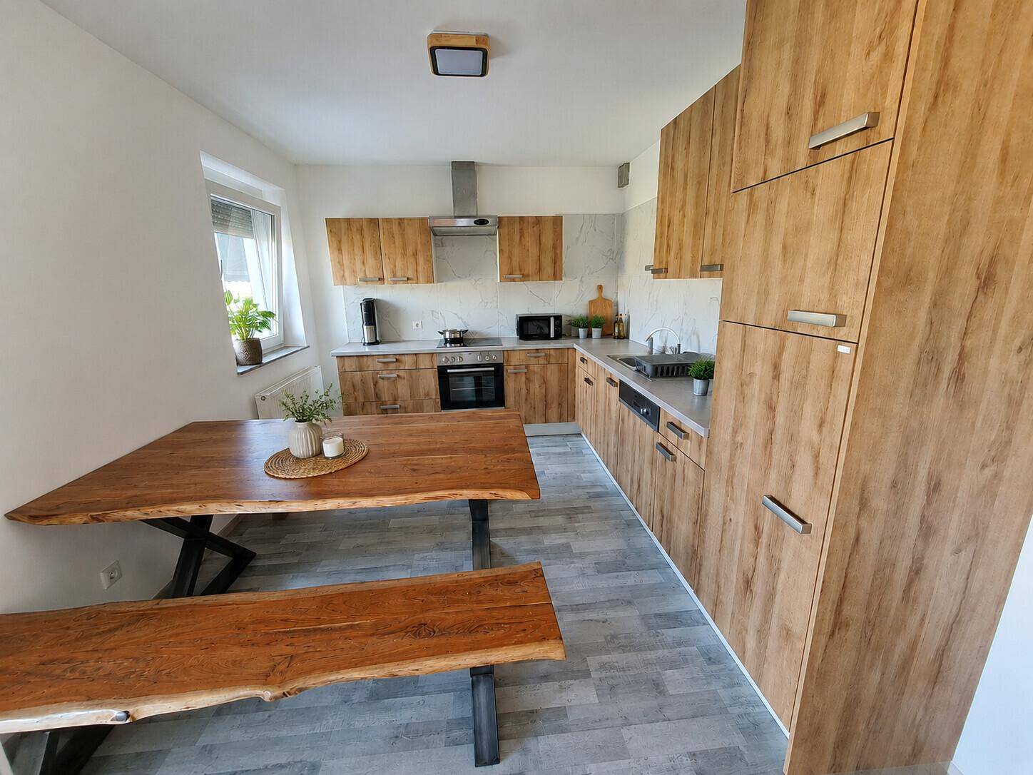 Moderne Wohnküche mit Holzelementen, großem Esstisch und integrierten Küchengeräten.