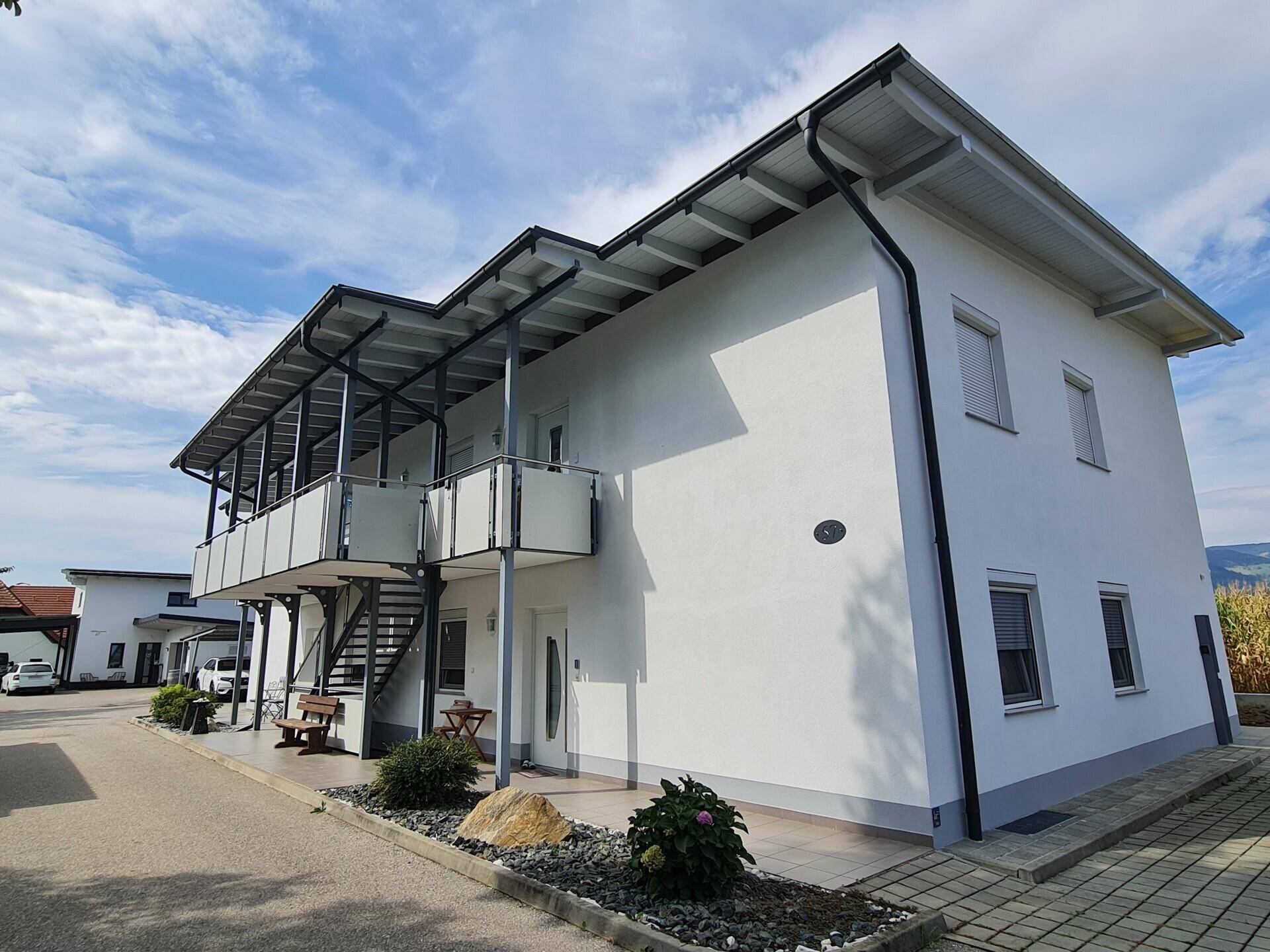 Modernes Mehrfamilienhaus mit weißer Fassade, mehreren Balkonen und Blick ins Grüne.