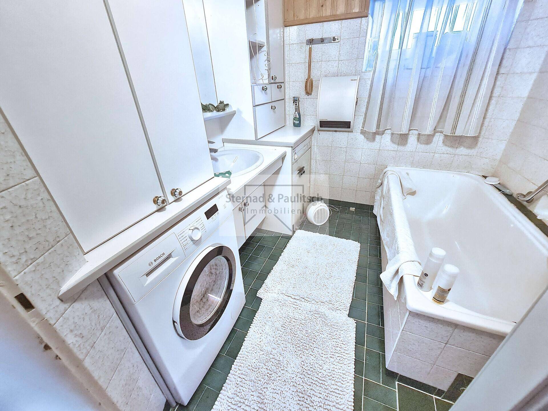 Badezimmer mit Badewanne, Waschmaschine, Waschbecken und grünen Fliesen.