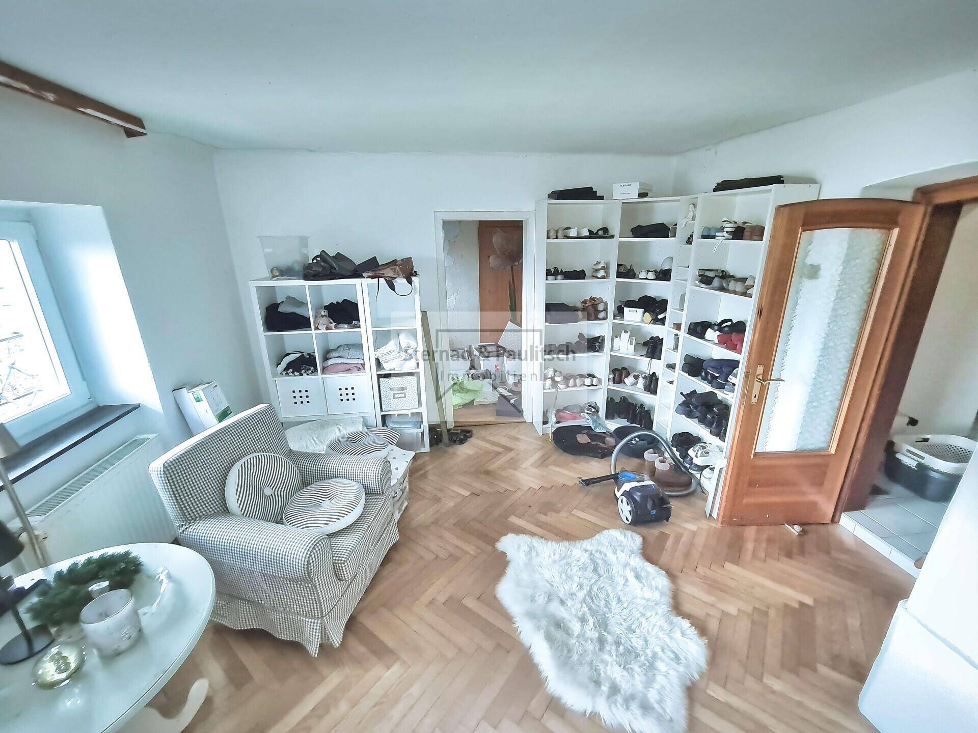 Raum mit Regalen für Schuhe und Kleidung, Holzboden und Fenster.