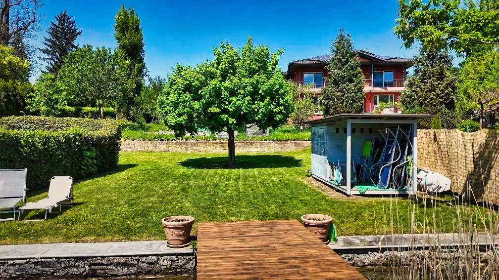 Großer Gartenbereich mit Rasen, altem Baum und direktem Zugang zum See mit eigenem Steg.