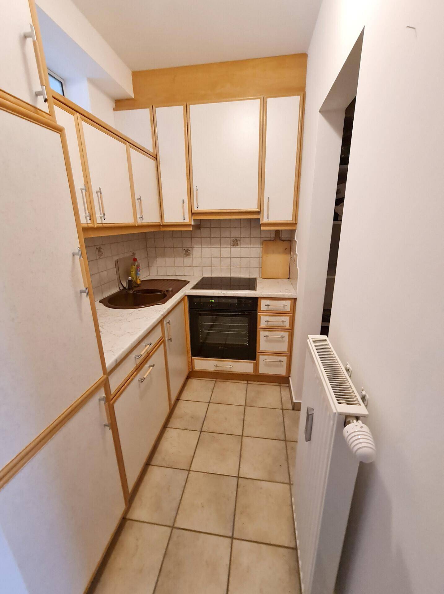 Funktionale Küche mit weißen und holzfarbenen Schränken, Fliesenboden und integriertem Backofen.