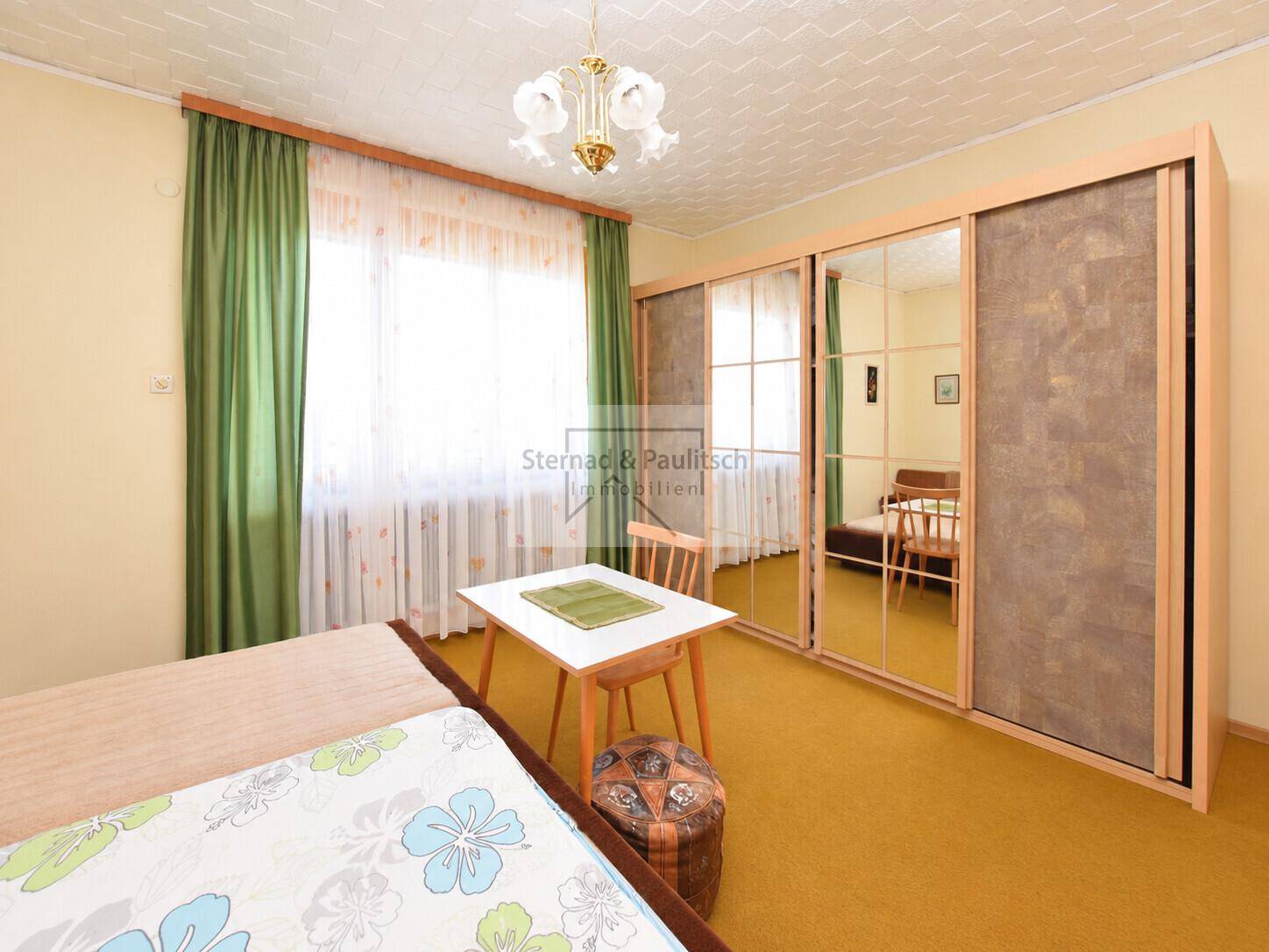 Schlafzimmer mit Spiegelschränken, Einzelbett und Fenster mit grünen Vorhängen.