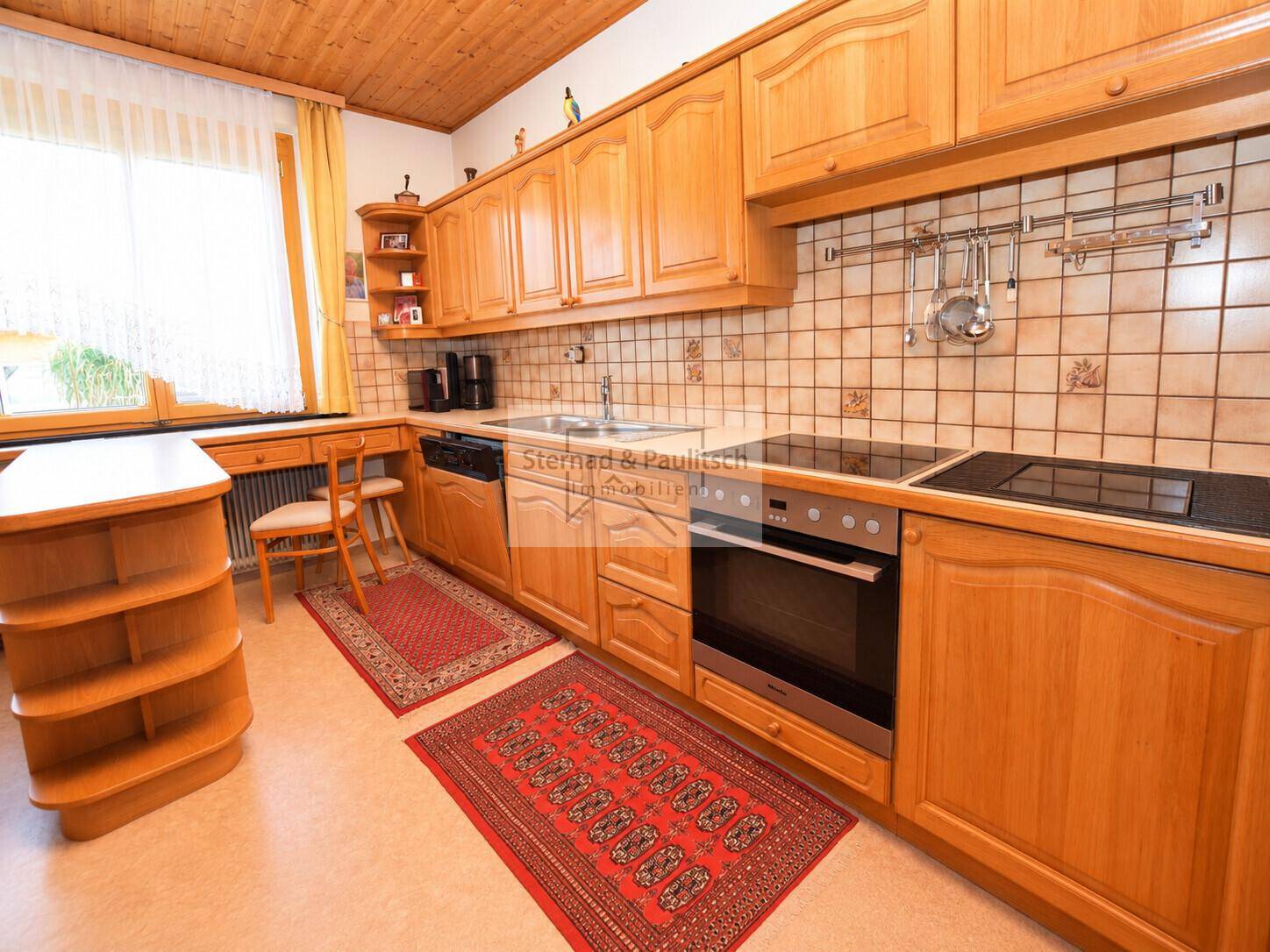 Funktionale Küche mit hellen Holzschränken, Fliesenrückwand und integrierten Küchengeräten.